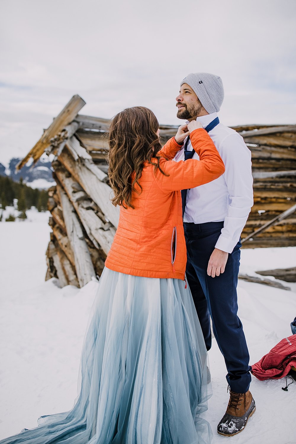 bride fixing grooms shirt and tie, winter elopement in breckenridge colorado, outdoor winter wedding, outdoor winter elopement, navy blue wedding colors, snowy winter wedding, colorado cabin relic