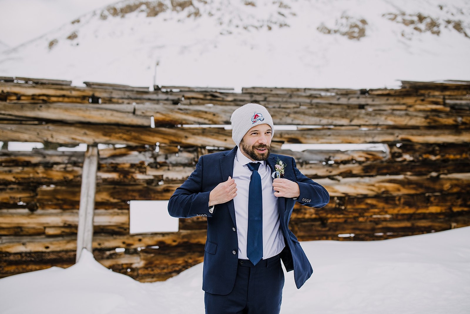groom putting on wedding jacket, groom getting ready in the snow, navy winter elopement colors, colorado avalanche beanie, winter wedding florals, winter elopement in breckenridge colorado