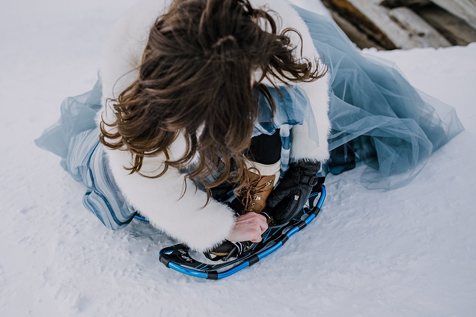 Bride strapping on snowshoes, blue wedding skirt, sorel wedding boots, snowshoe wedding, snowshoe elopement, breckenridge snowshoe elopement, yukon charlie snowshoes