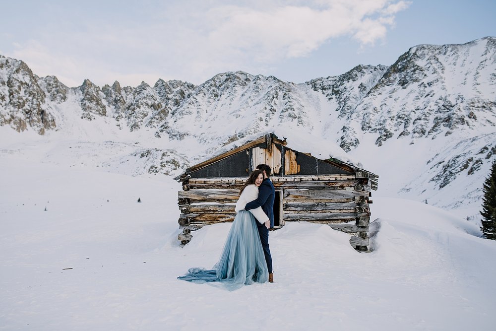 Bride grabbing groom in front of log cabin, kiss in front of mining cabin, kiss in ghost town, leadville mining history, snowshoe to atlantic peak, kiss in front of quandary