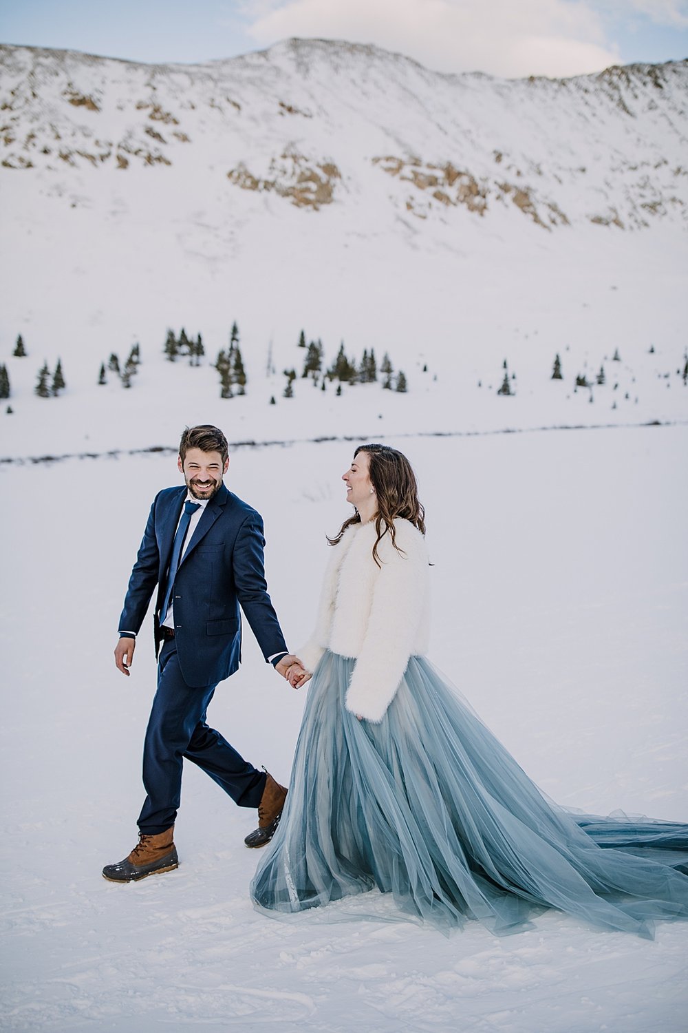 bride and groom walking hand in hand through the snow, snowy walk, winter elopement hiking boots, winter wedding hiking boots, blue grooms tie, blue wedding tie