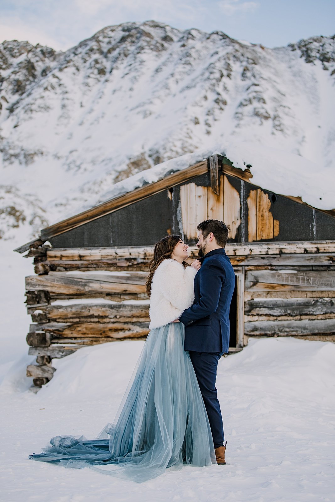 Groom with hands on brides waist, grooms holds bride in front of cabin, mining elopement, winter mining cabin elopement, leadville winter snowshoe wedding