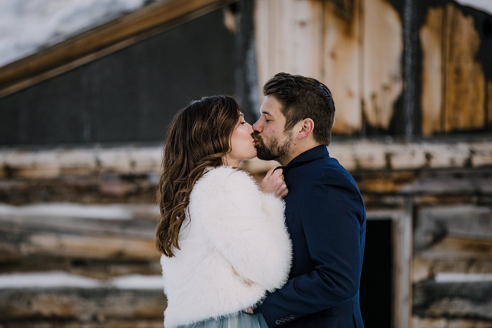 Couple kissing in front of mining cabin, bride and groom snuggle in the mountains, snowy snowshoe adventure, snowy snowshoe elopement, kiss in front of cabin