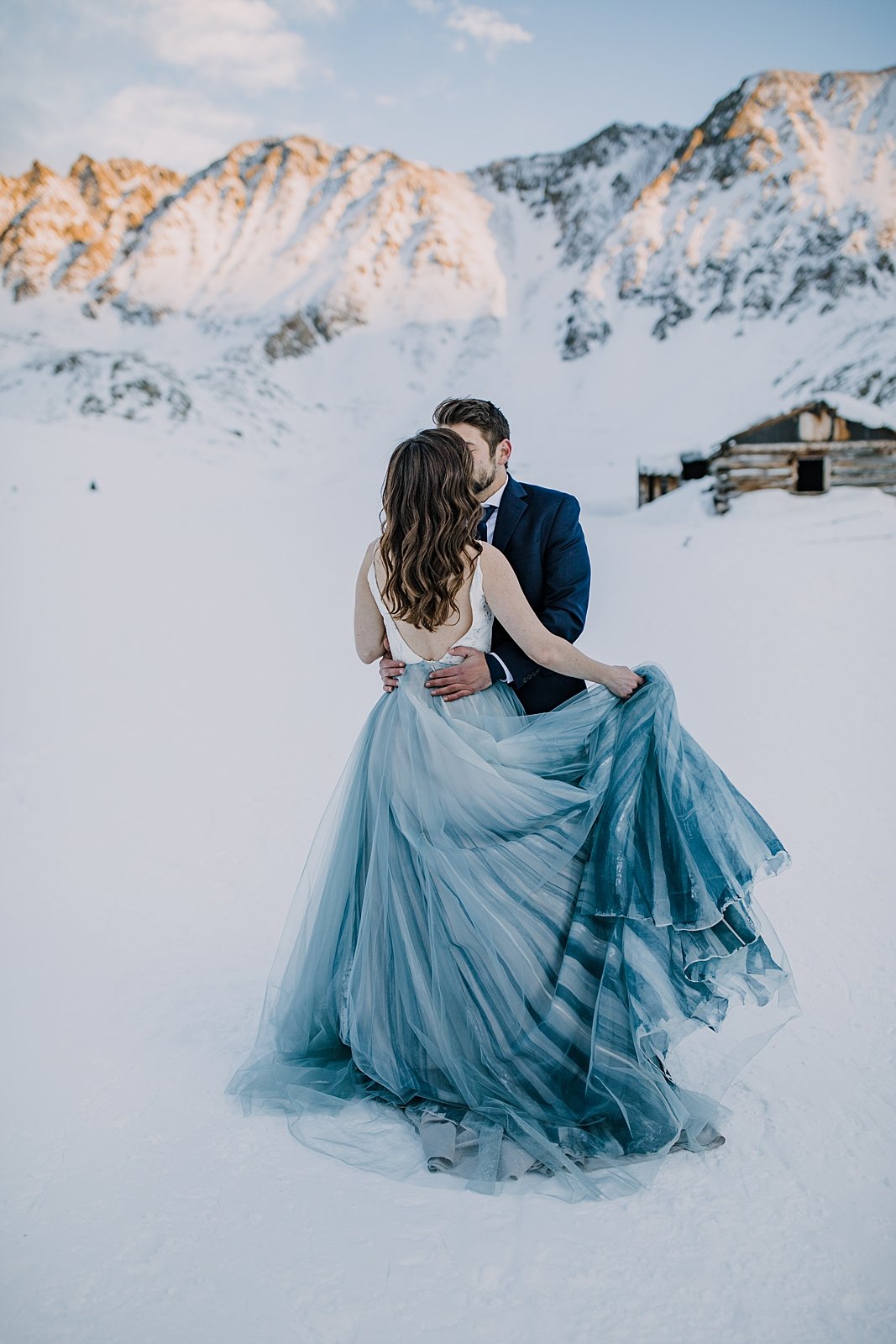 bride and groom kissing in the snow, painted blue wedding skirt, winter elopement hiking boots, winter wedding hiking boots, winter alpenglow in mayflower gulch, sunset in mayflower gulch
