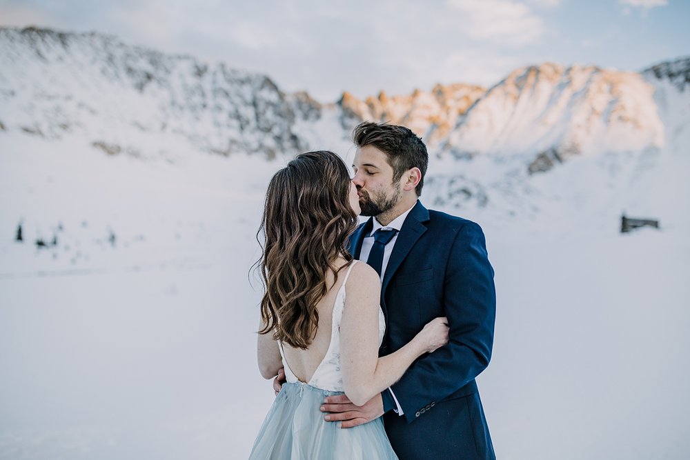 bride and groom kissing in front of mountain view, mountain alpenglow wedding, mountain alpenglow elopement, winter alpenglow elopement, fletcher mountain alpenglow