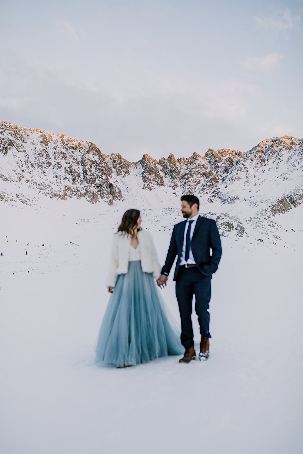 bride and groom walking hand in hand through the snow, snowy walk, winter hiking elopement, winter wedding in leadville colorado, elopement surrounded by mountains, alpenglow over colorado mining town