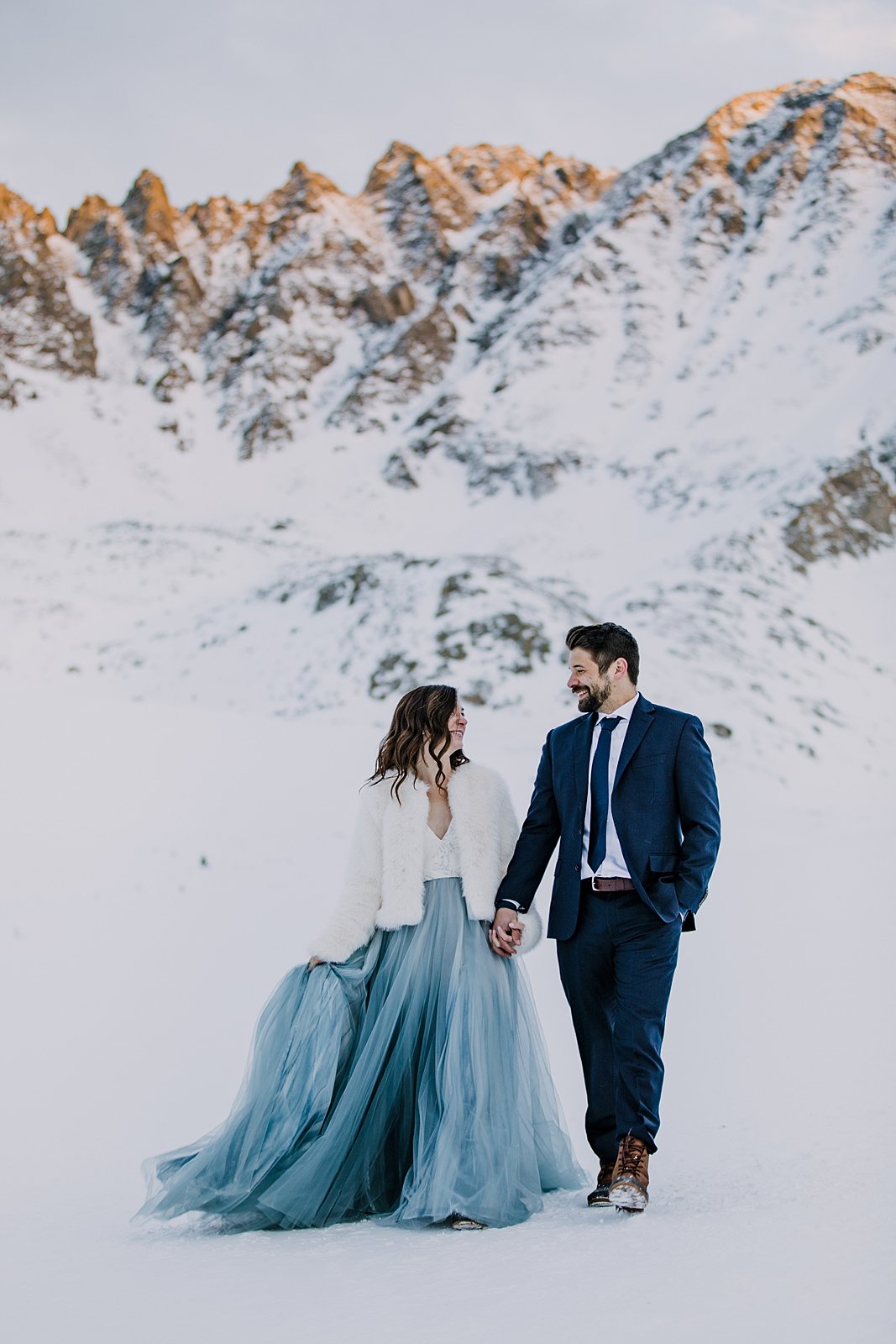 bride and groom walking hand in hand through the snow, snowy walk, winter elopement hiking boots, winter wedding hiking boots, walk in the woods, alpenglow over colorado mining town