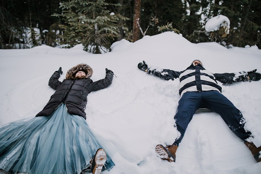 bride and groom laying in the snow making snow angels, colorado snow angels, outdoor winter forest wedding, outdoor winter wooded elopement, outdoor winter forest elopement