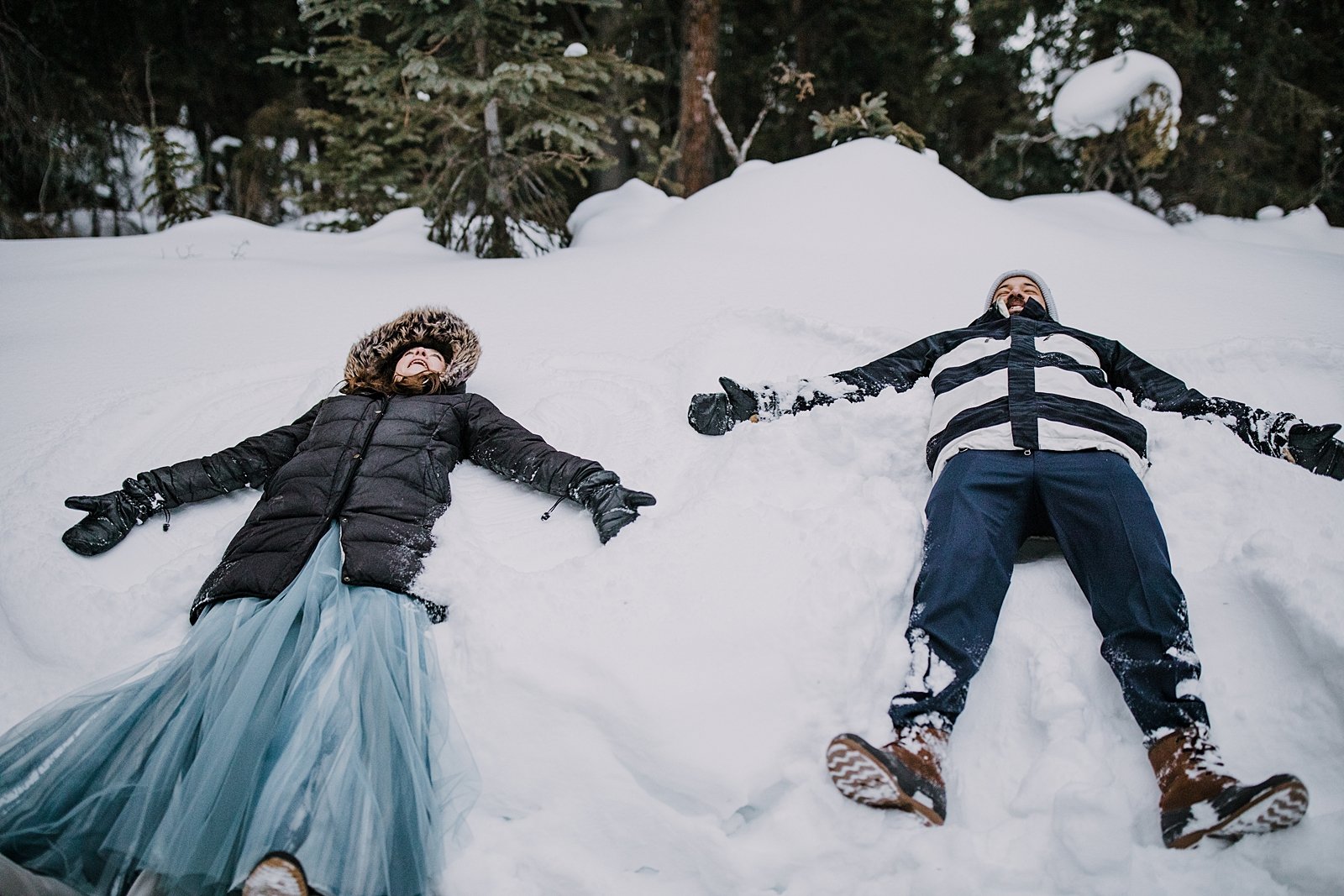 bride and groom laying in the snow making snow angels, colorado snow angels, outdoor winter forest wedding, outdoor winter wooded elopement, outdoor winter forest elopement