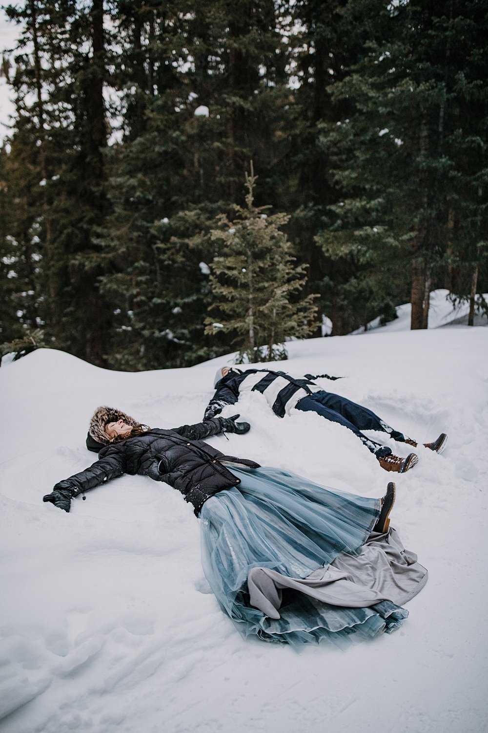 bride and groom laying in the snow making snow angels, colorado snow angels, outdoor winter forest wedding, outdoor winter wooded elopement, outdoor winter forest elopement