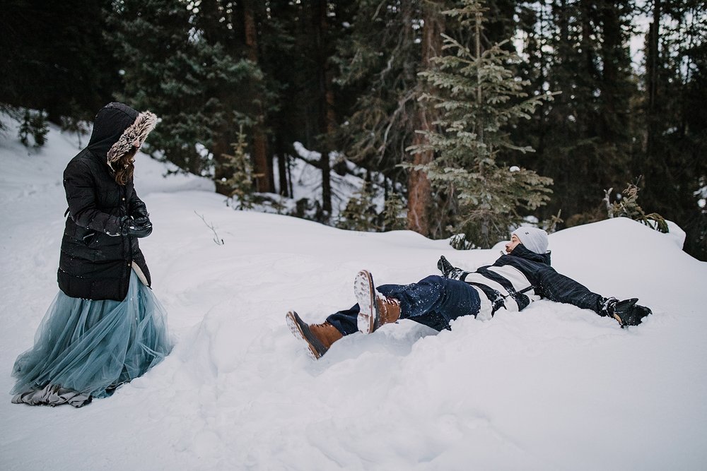 bride and groom playing in the snow, snow angels on trail, colorado snow angels, snowy winter forest wedding, snowy winter forest elopement, bride and groom snowball fight