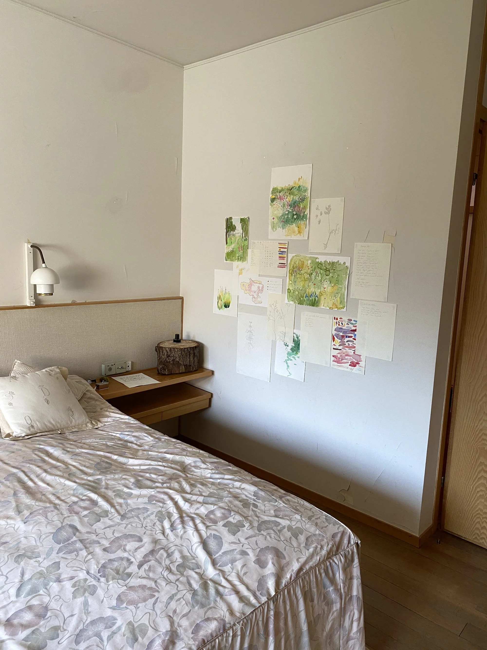 A bedroom at Maison Louis Carré with watercolours and drawings on the wall and a tree stump on the bedside table