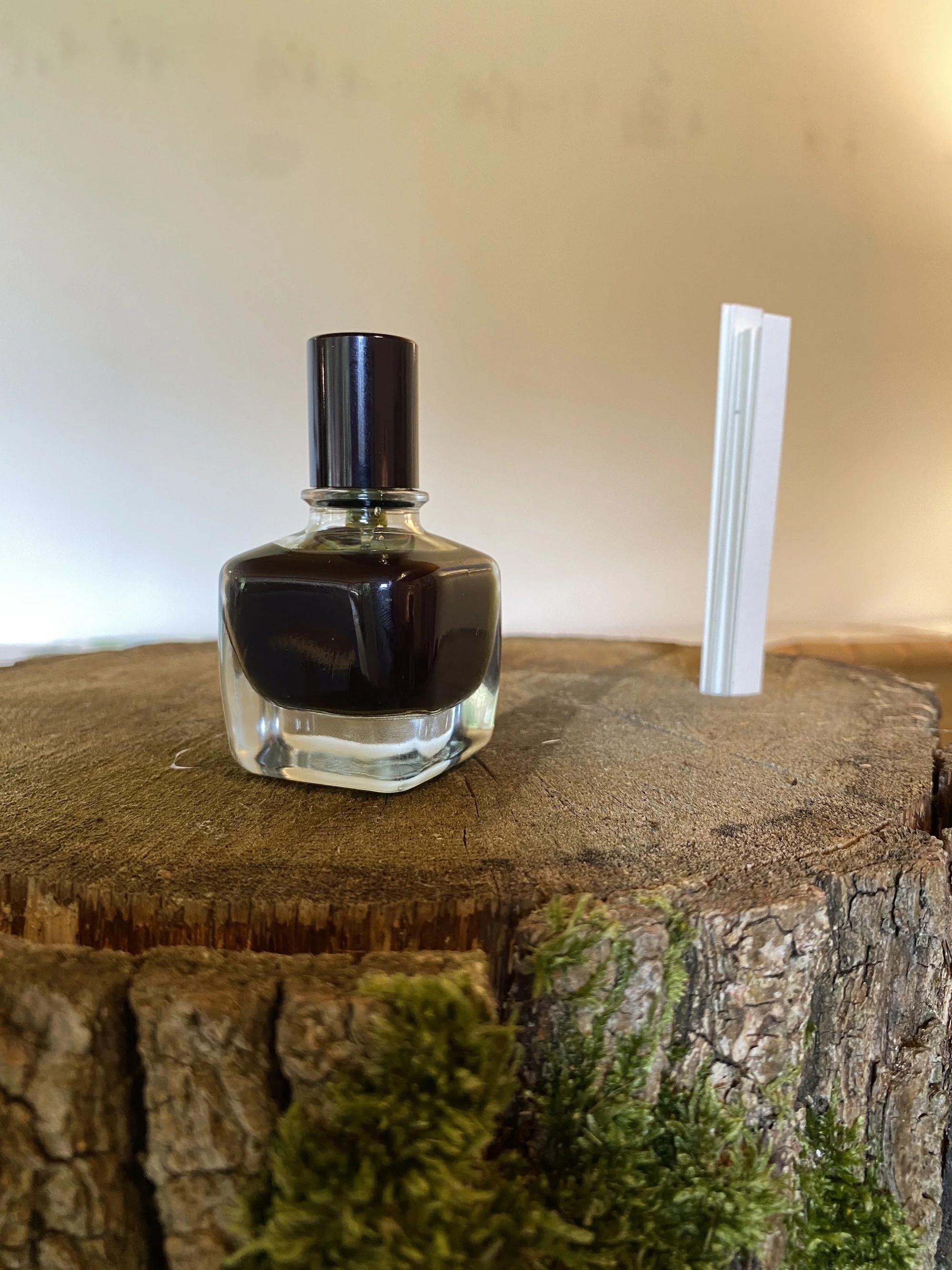 A perfume bottle of dark scent and paper scent strips on a tree stump with moss