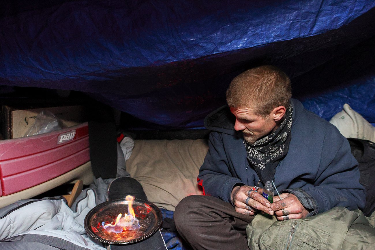 Nik warms himself with a fire created from hand sanitizer, rubbing alcohol and candlewax. He said the mixture creates less smoke than other fires. Credit: Giles Clasen