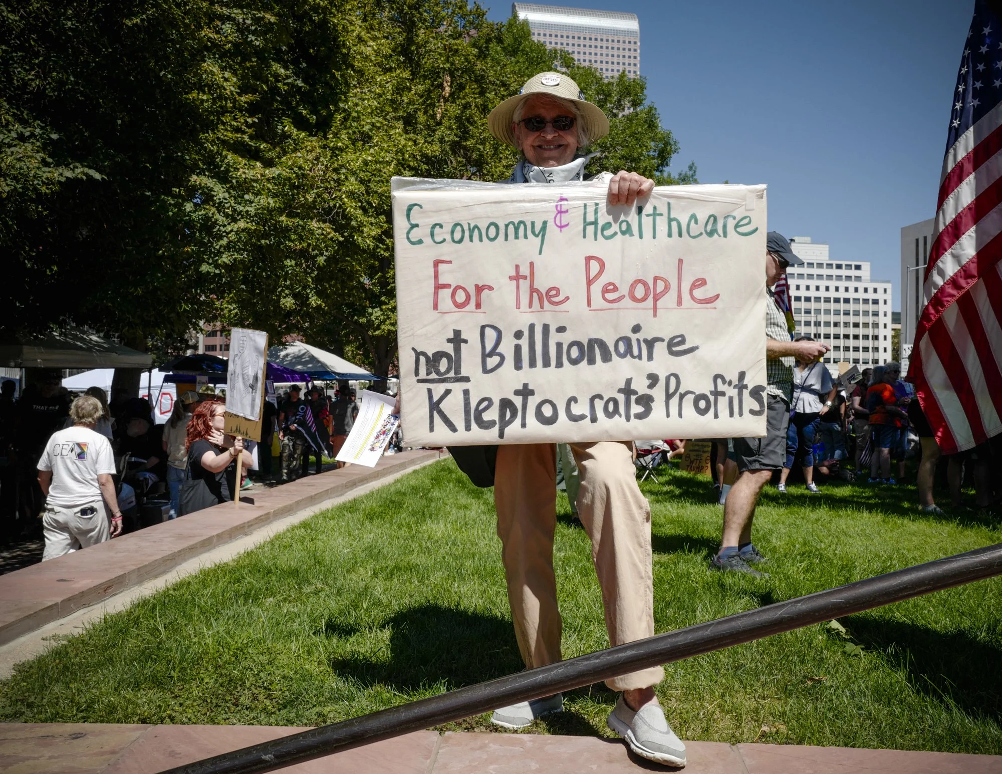 Michele Swenson holds a sign that reads "Economy & Healthcare For the People, not Billionaire Kleptocrats' Profits."