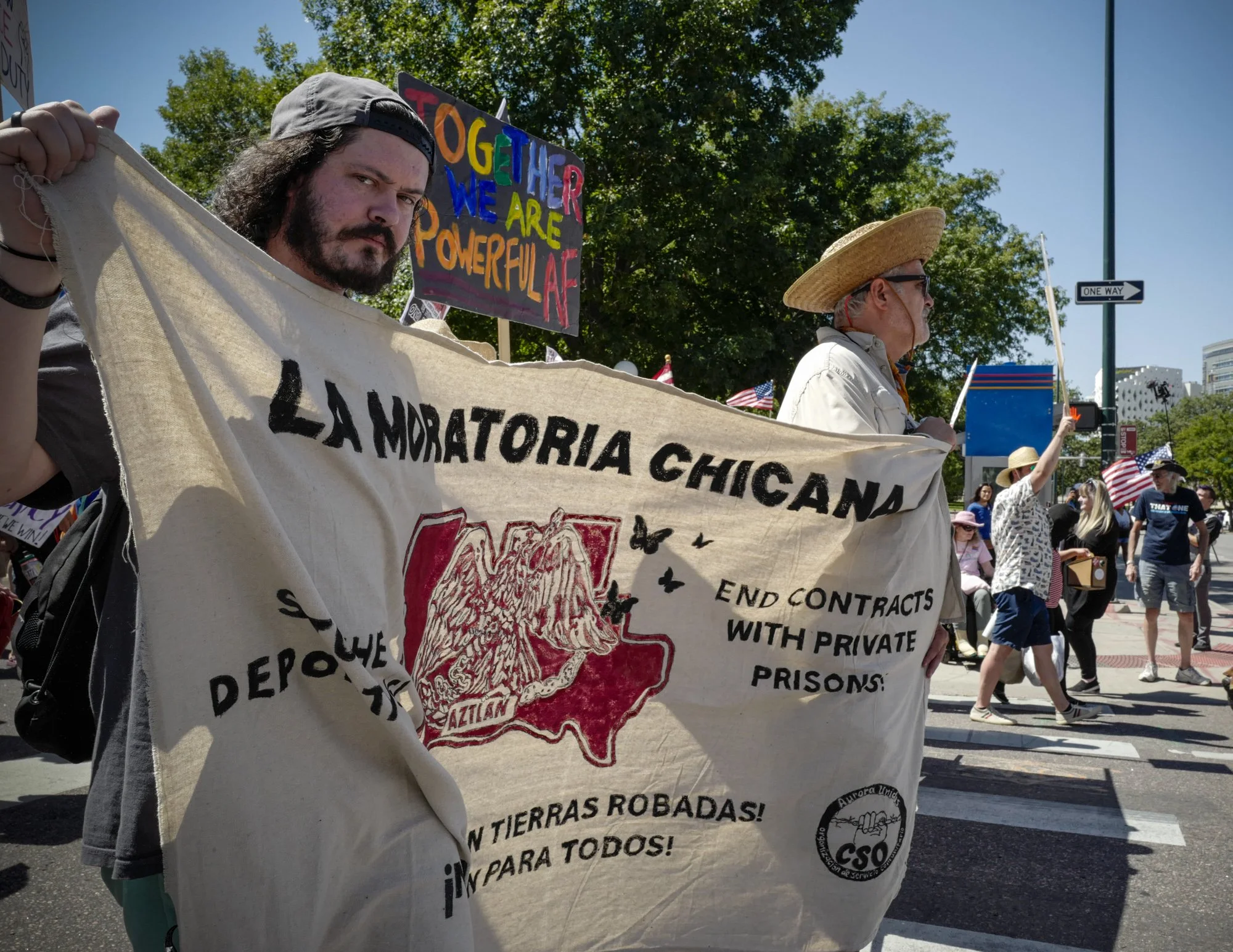 A protester carries a banner for "LA MORATORIA CHICANA," calling for the termination of contracts with private prisons, as they march with others.
