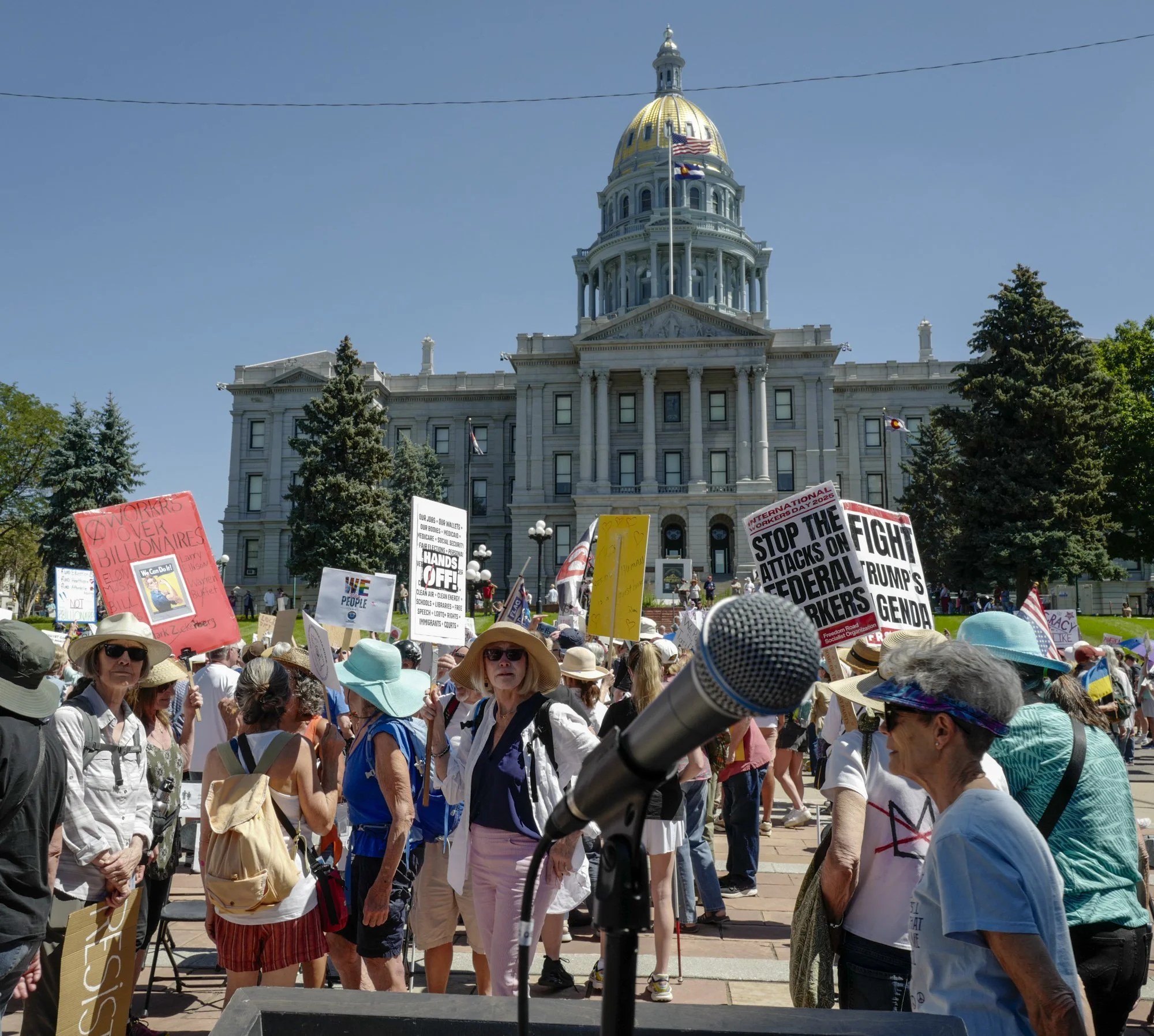 Marchers gathered in front of the Colorado State Capitol building, with multiple protest signs visible.