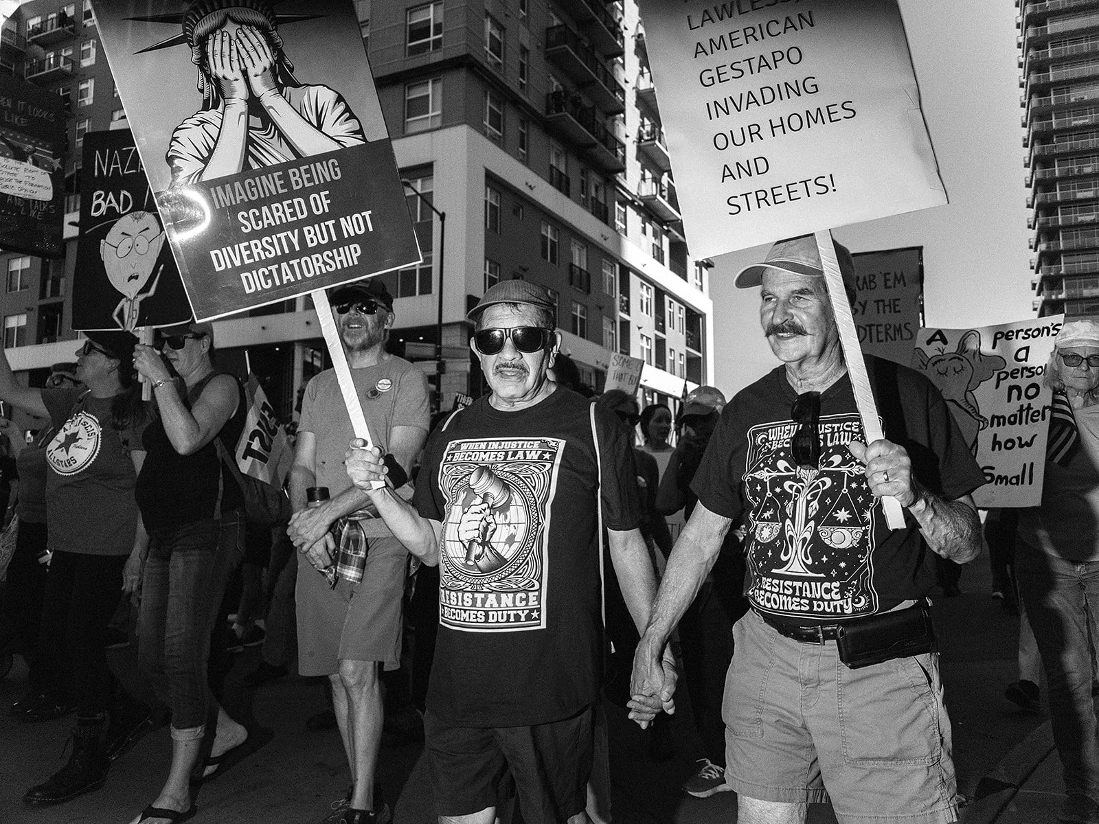  Participants carrying signs walk hand in hand through downtown Denver during the No Kings march on Saturday, Oct. 17, 2026. Photo by Jeff Tidwell for the Denver Voice.