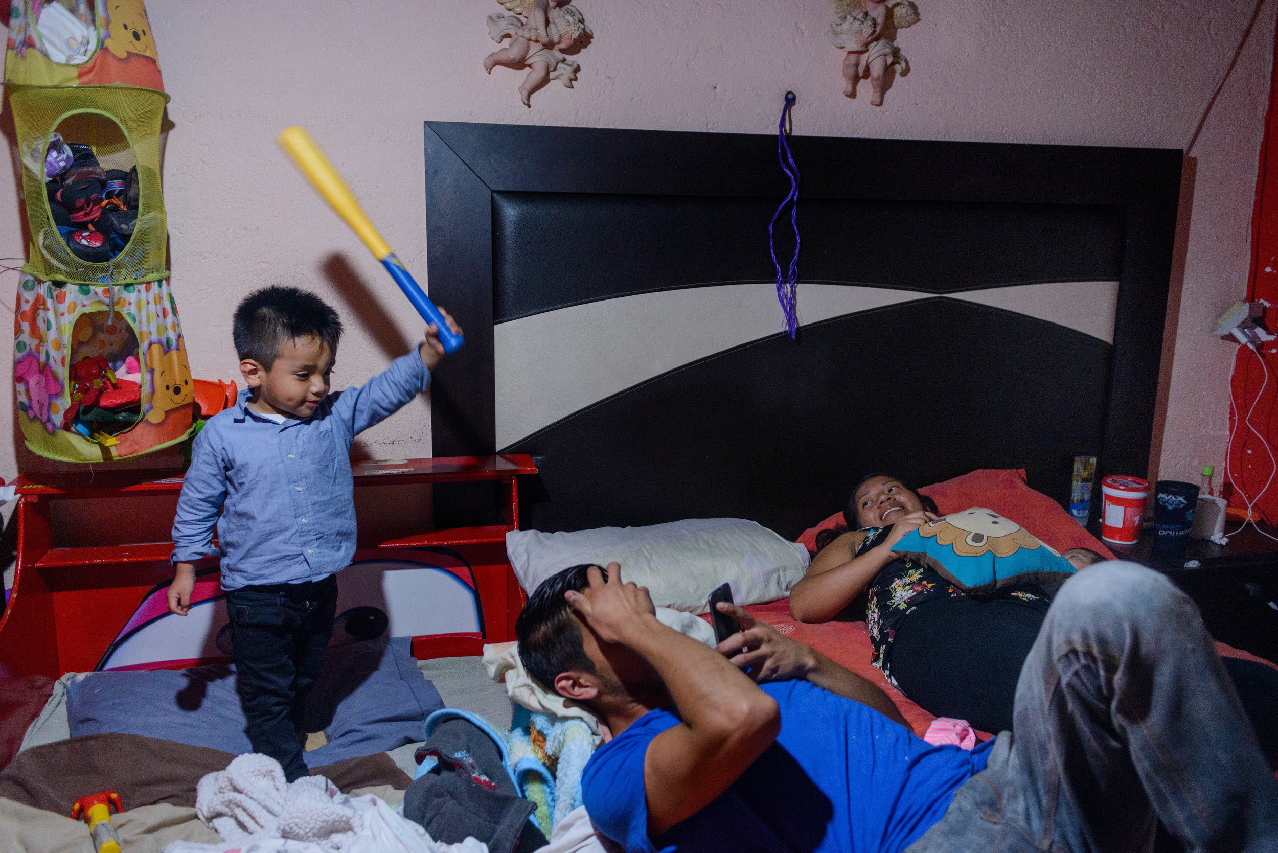  3 year old Logan threatens to hit his father with a play bat while his mother Marlen enjoys a moment of rest with her 2-month old daugher. 