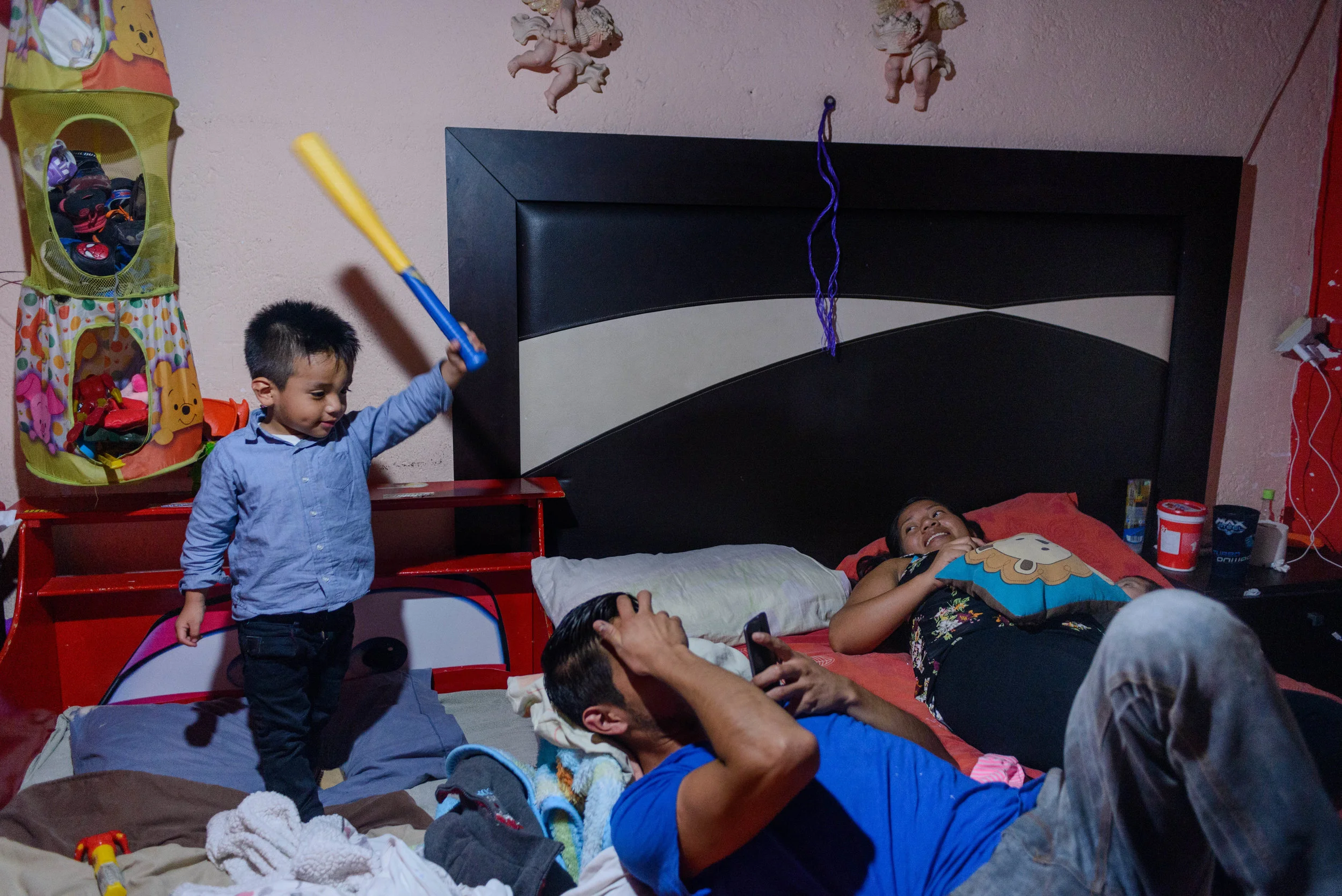 3 year old Logan threatens to hit his father with a play bat while his mother Marlen enjoys a moment of rest with her 2-month old daugher.