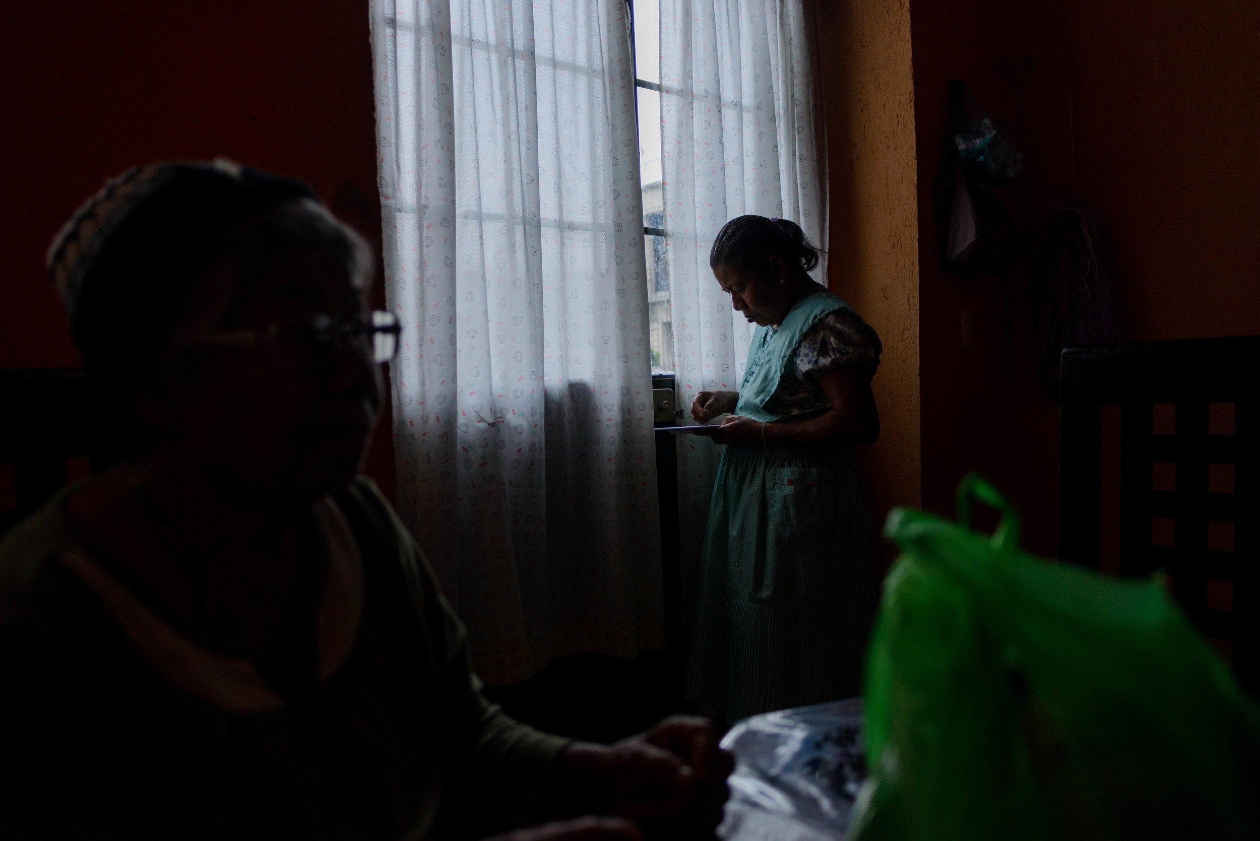  Agustina Marcos tells a story while her daughter and craftswoman Hermenegilda Ascenio Marcos looks at her food under the window light in the background. 