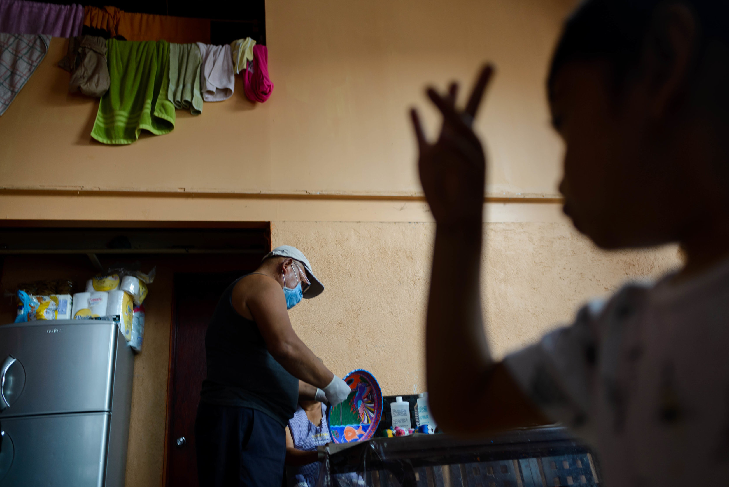  3 year old Jael dances in front of the TV and looks over at his grandfather Juan who is varnishing the bowls he has recently handpainted. 