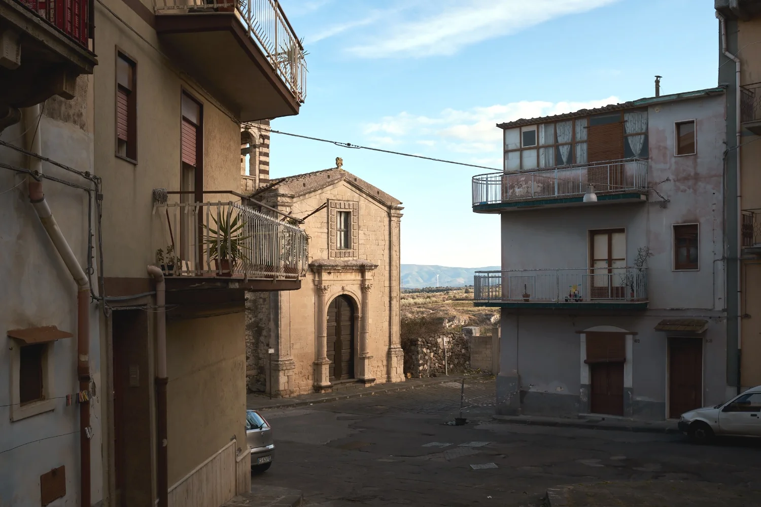 Casa mia Militello in Val di Catania en Sicile, le village de mes parents, d’où ils ont émigré et où ils sont retournés. Je connais ce lieu depuis toujours par leurs mémoires, leurs récits, nos visites et mes voyages. Mes origines sont en Sicile, c’est ma terre, mais le village c’est chez mes parents, pas chez moi. J’ai besoin d’y aller chaque année, et une fois sur place je m’y ennuie. De l’ennui, de la tendresse et des questions qui m’ont amené à photographier ce village comme on parcourt adulte la maison de son enfance. Attendre le retour En hiver, rien ne se passe, c’est figé, seuls les vieux sont dehors. Les autres sont partis travailler ailleurs et ils seront de retour, plus tard. Je me suis aventuré dans les rues et les cafés au cours de promenades, un reportage sans but précis, plus une pratique qu’un objectif. J’ai capté des sensations et des instantanés en laissant de côté ma technique photographique et en cherchant ma place dans ces temps de l’intime. Attendre l’arrivée Les processions de Santa Maria della Stella , des 8 et 9 septembre animent Militello in Val di Catania. Les immigrants sont de retour, les touristes et visiteurs nombreux. La place centrale est noire de monde et tous attendent la sortie de la Vierge pour la procession qui se déroule du parvis de l’église Santa Maria aux ruelles du bourg. Tirs de canon, confettis et guirlandes bianco blu , le village se prépare et se colore pour se célébrer. Sacrées et folkloriques, ces processions sont déjà connues, documentées et photographiées. Je ne voulais pas montrer ce cortège ou ses protagonistes mais son intensité et son rythme pour moi. J’ai pris le regard de ceux qui y assistent, cherchant ma place dans la foule et les temps morts de l’été festif. Attendre, trouver sa place, trouver la bonne distance. Extrait de l’exposition Casa Mia présentée au cafe du tunnel.
