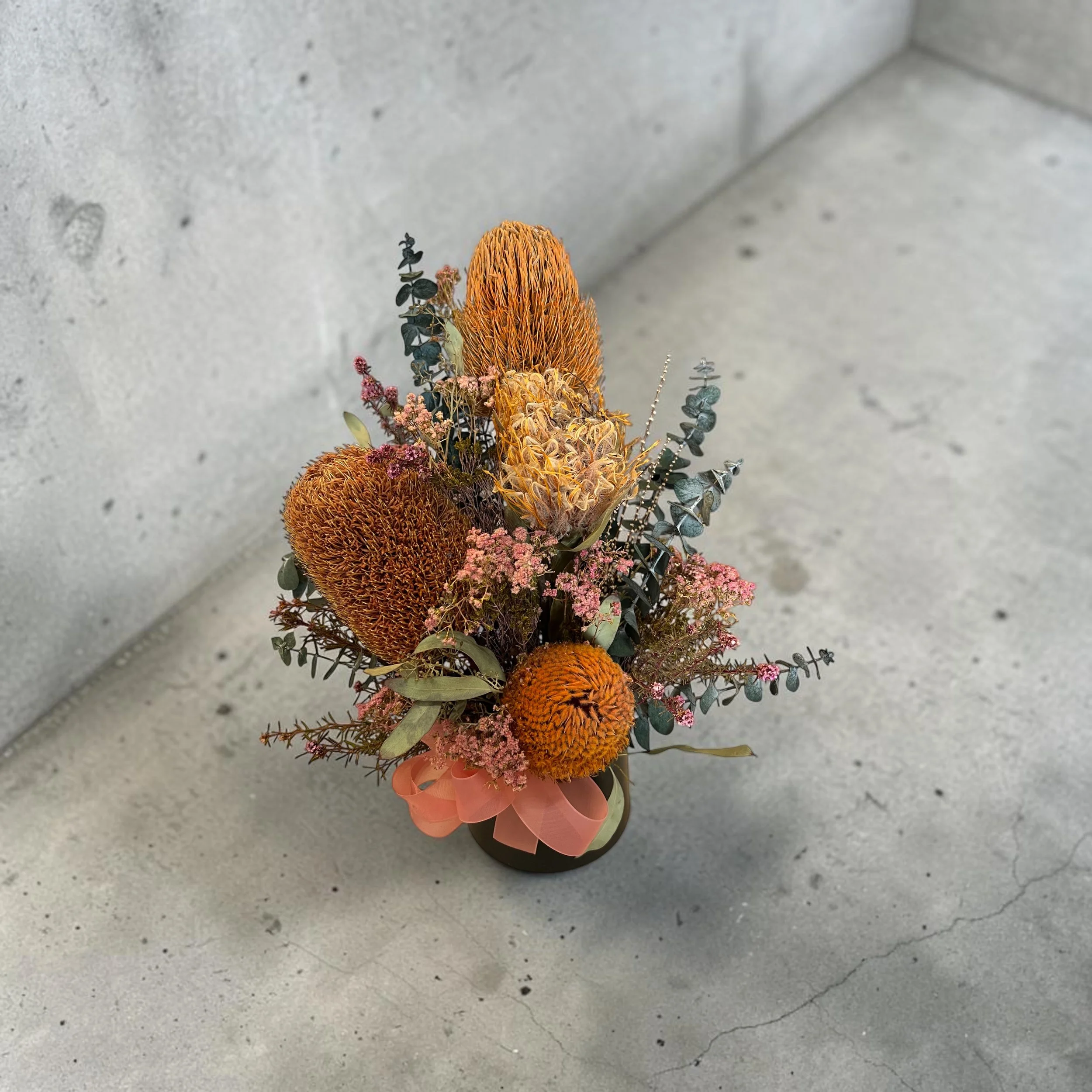 dried native flower arrangement in orange &amp; pink tones on background