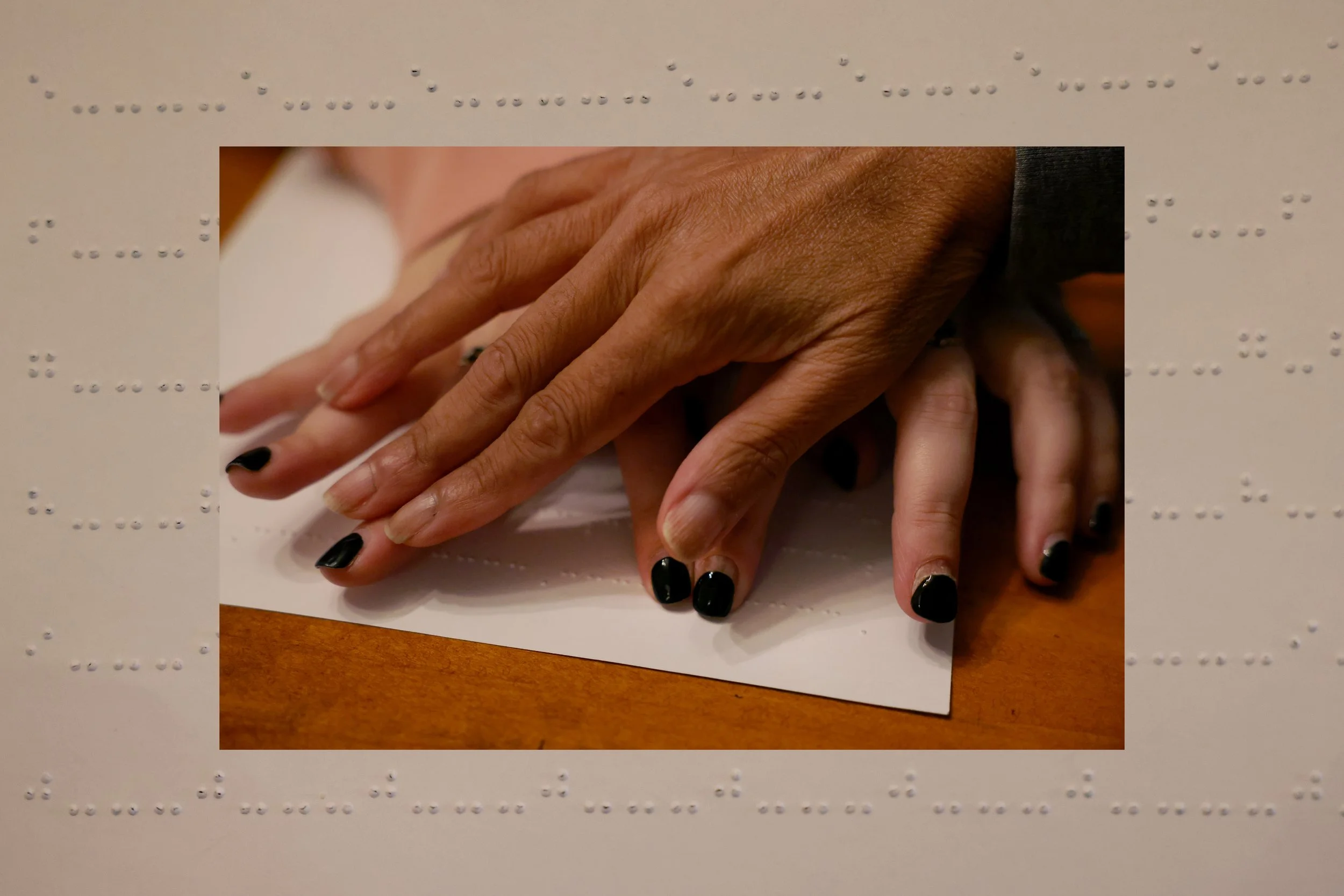 Nisha Falcigno uses her braille instructor’s hands to guide her through the raised tactile letters on the page during a braille lesson in her Manhattan apartment on Nov. 14, 2023. 