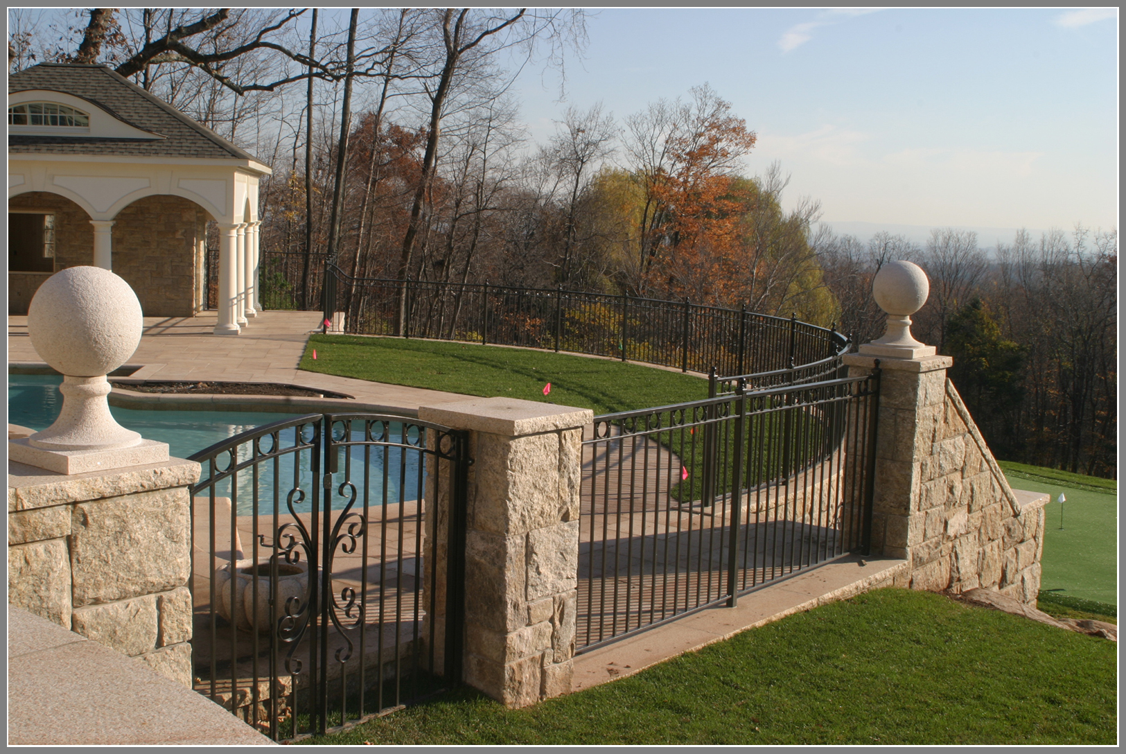 Wrought iron pool fence with stone columns by Artistic Outdoors