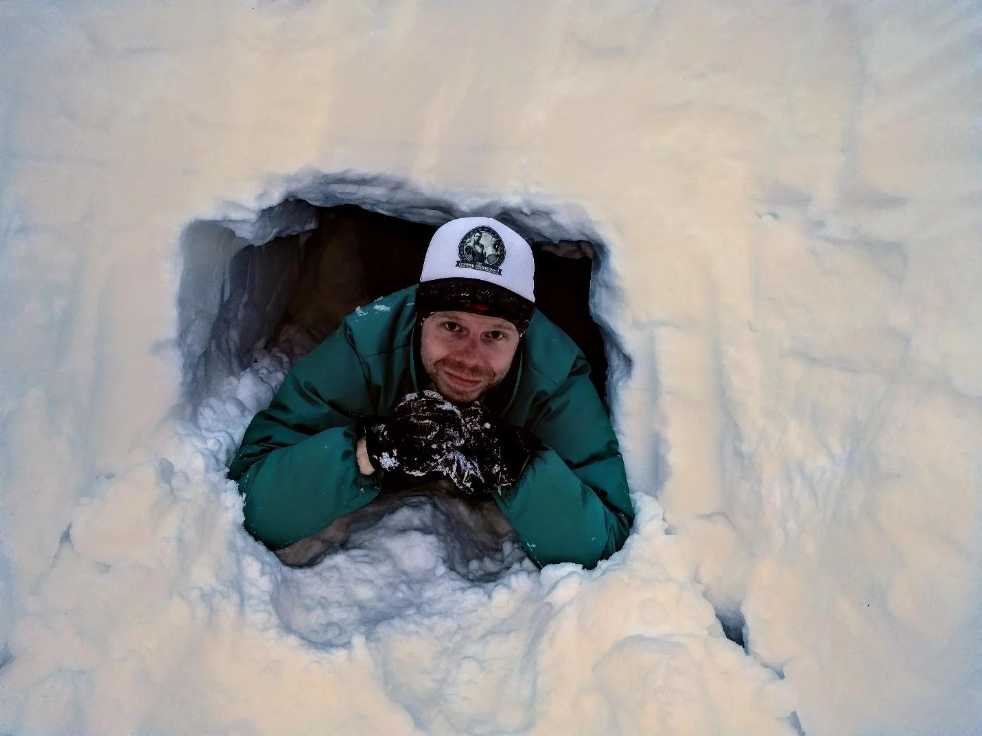Brian lounges in the quinzhee entrance. It should be noted that he opted to not sleep here for fear his white ball cap would be lost in the white snow. Photo by Brian.