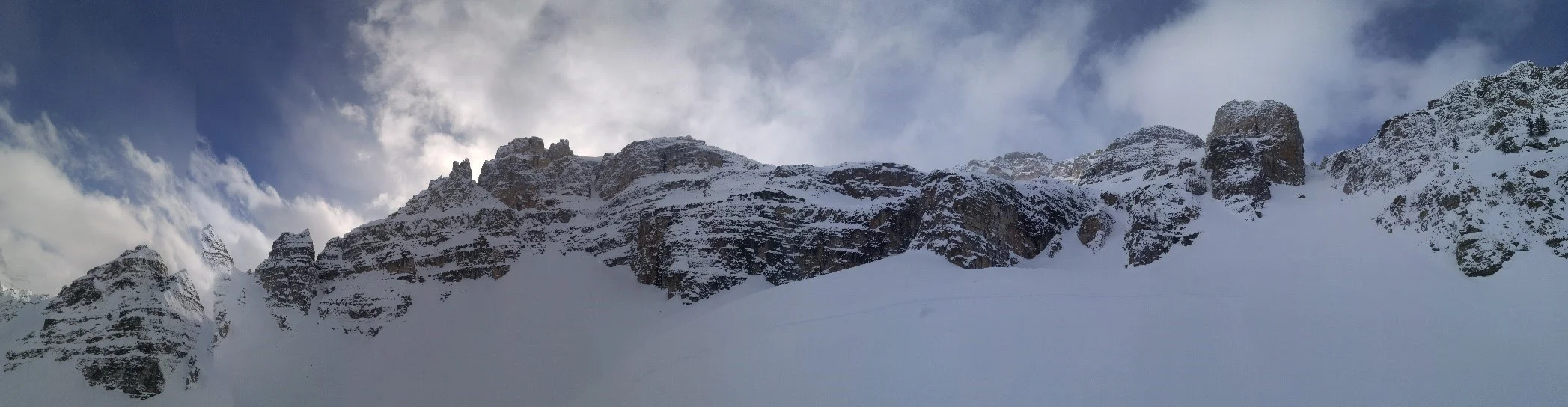 Panorama shot from the basin below Vanguard Peak/South Couloir. South couloir is on the right side of picture. From above, the more tempting descent would take you above the cliffs just lookers left of the South Couloir. At the very least it would mean mandatory air into a tight shoot, or a short rappel. Worst case scenario could involve cliffing out on some very large ledges. This panorama picture also explains why bootpacking up the south couloir is the only way out of the basin and is recommended in Summits and Icefields. If you are also in a position of looking for the couloir without having boot packed up it, make sure you get it right.