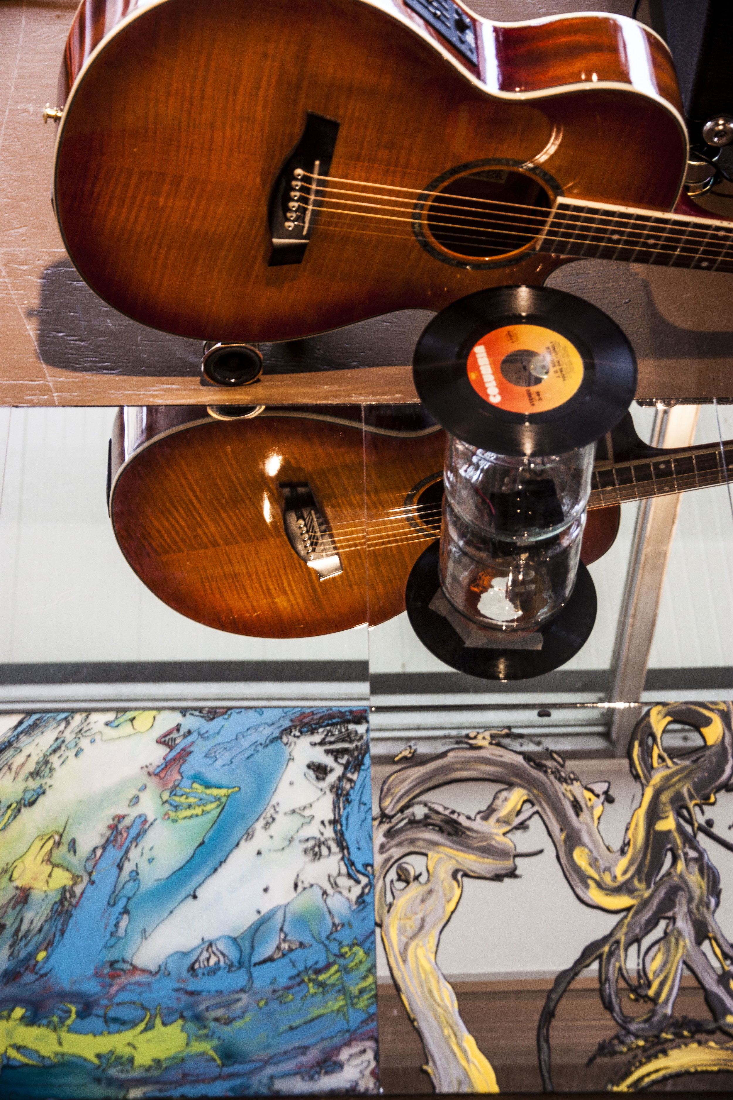  A drinking straw whirs atop a glass jar, powered by a DC motor  It strikes the strings of an acoustic guitar, which is reflected in the painted and un-painted mirrors beside it 