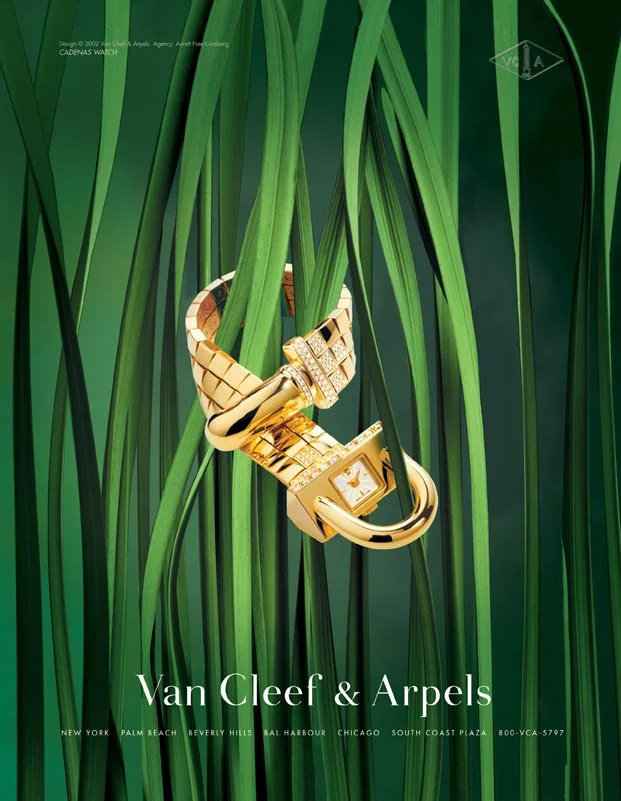 Gold jewelry, including a watch and a bracelet, entwined with green grass blades in a fashion advertisement for Van Cleef & Arpels.