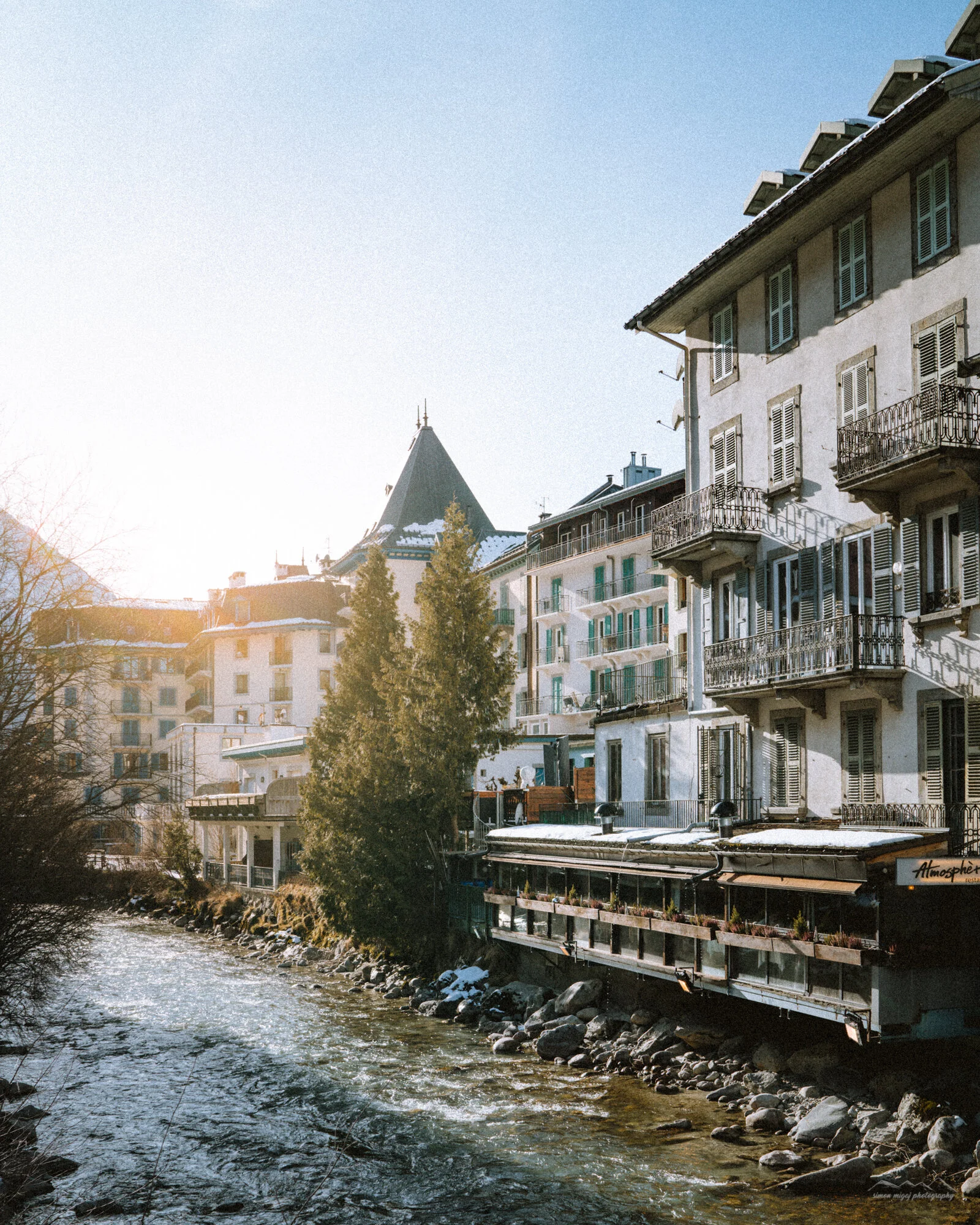 Studio apartment with balcony in an urban setting, overlooking a river, with snow on the ground and trees.