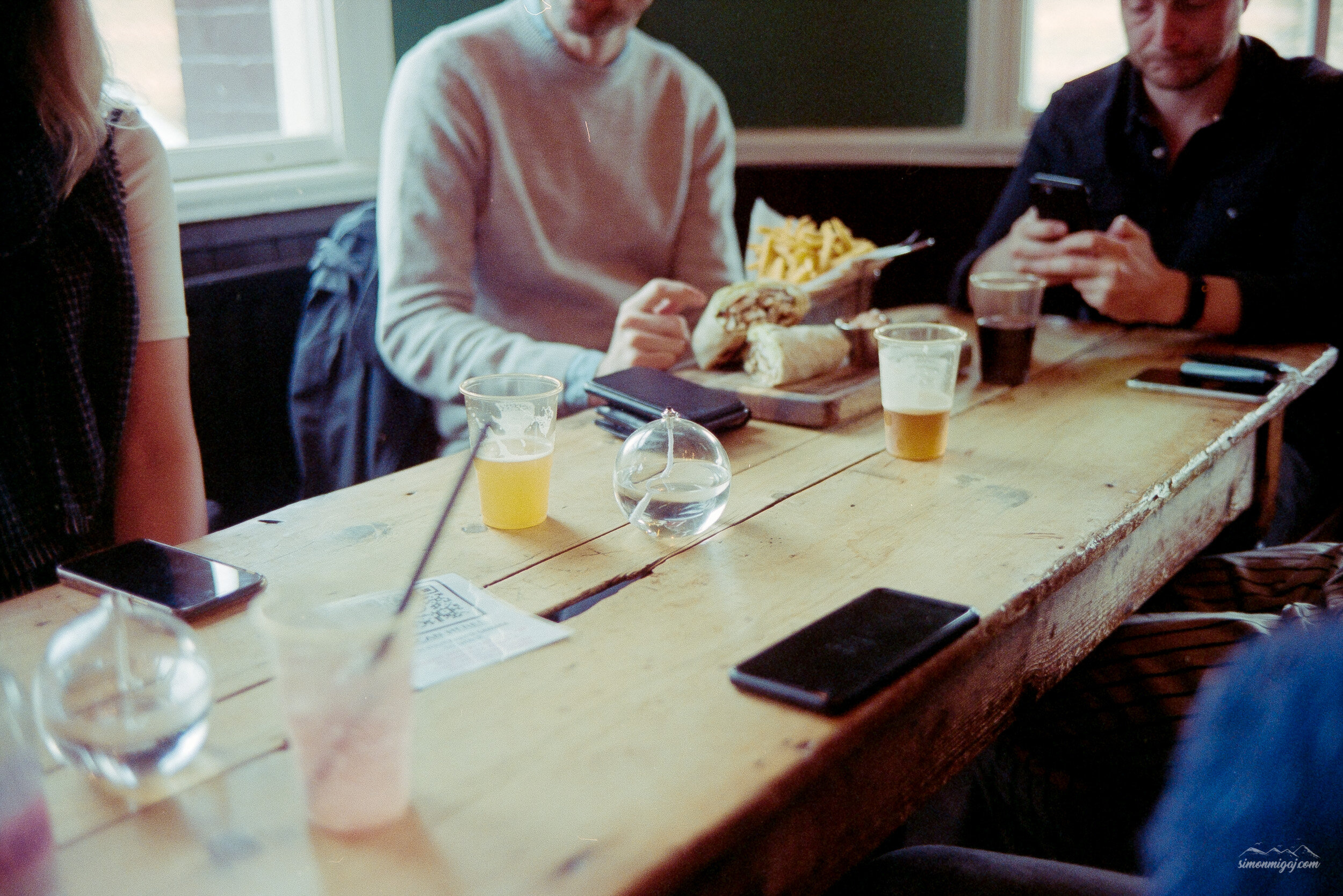 People sitting around a wooden table with drinks, papers, and food in a cozy indoor setting.