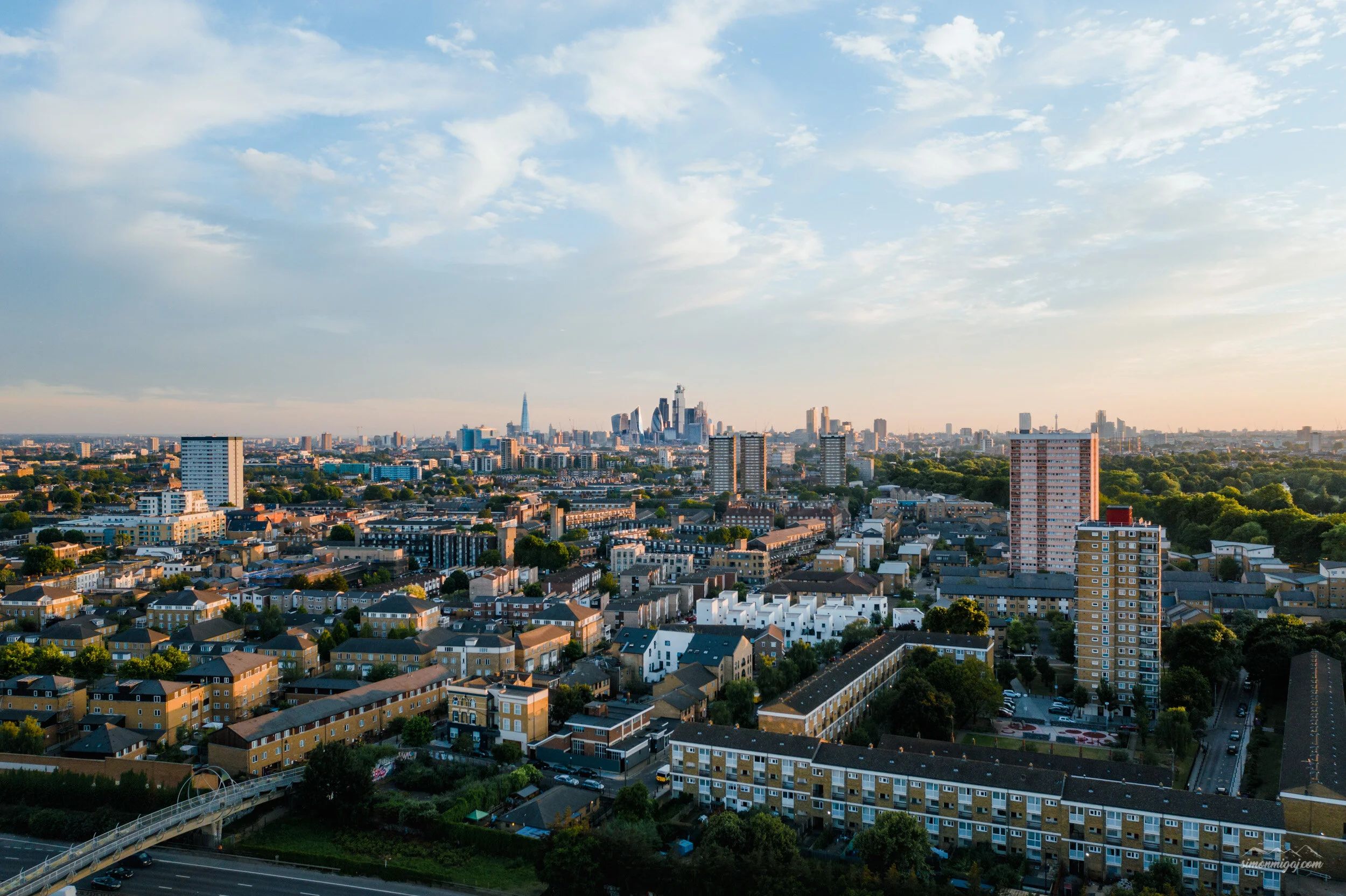 View of a city skyline with tall skyscrapers in the distance, residential buildings in the foreground, and a partly cloudy sky overhead.