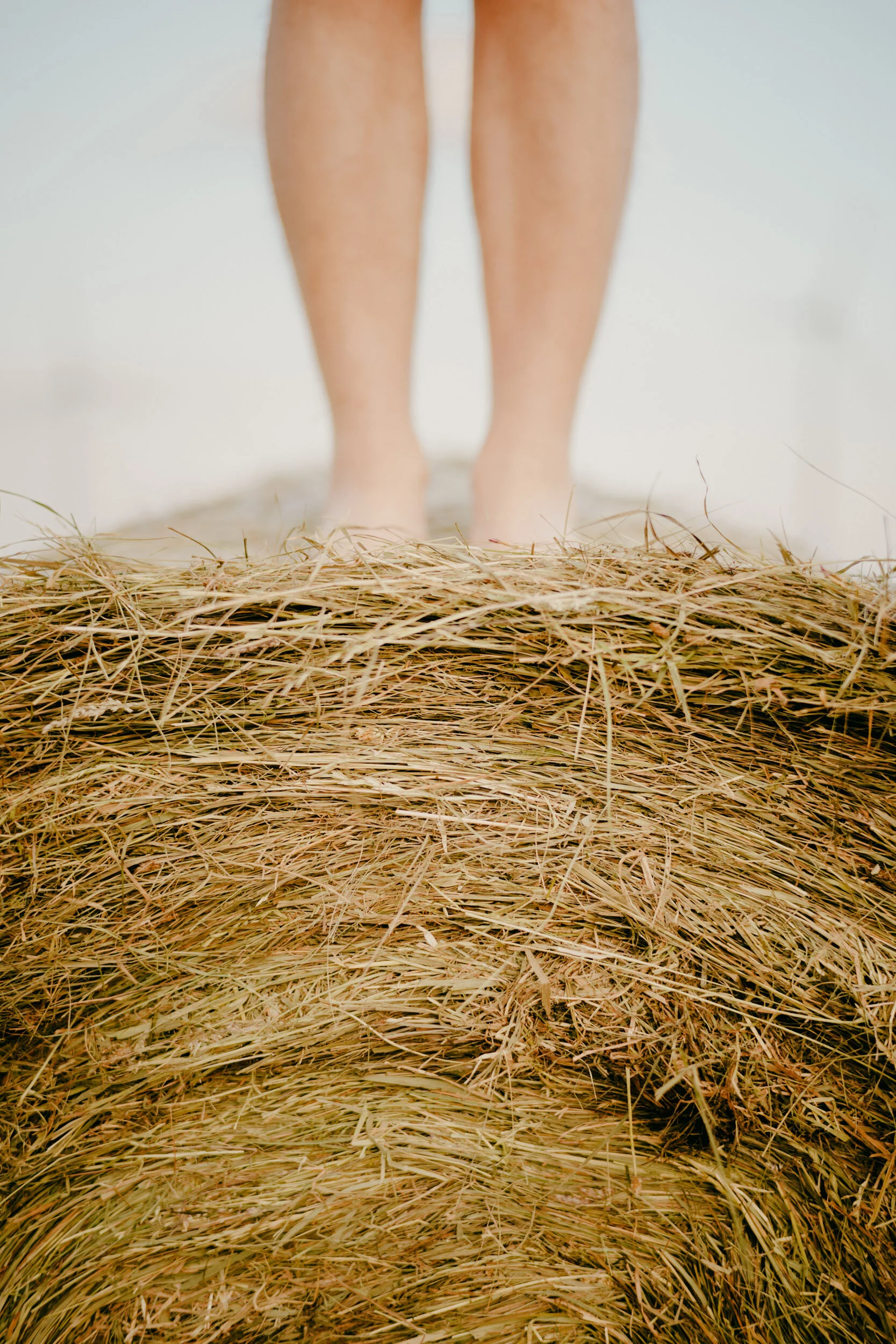 Person standing on a stack of hay or straw, with only their legs and feet visible in the image.