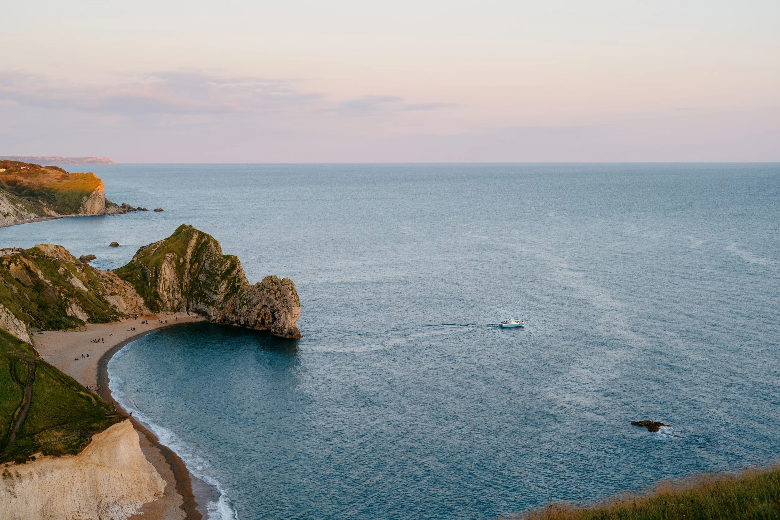 Cliffs by the ocean with a small beach and boat in the water, under a cloudy sky