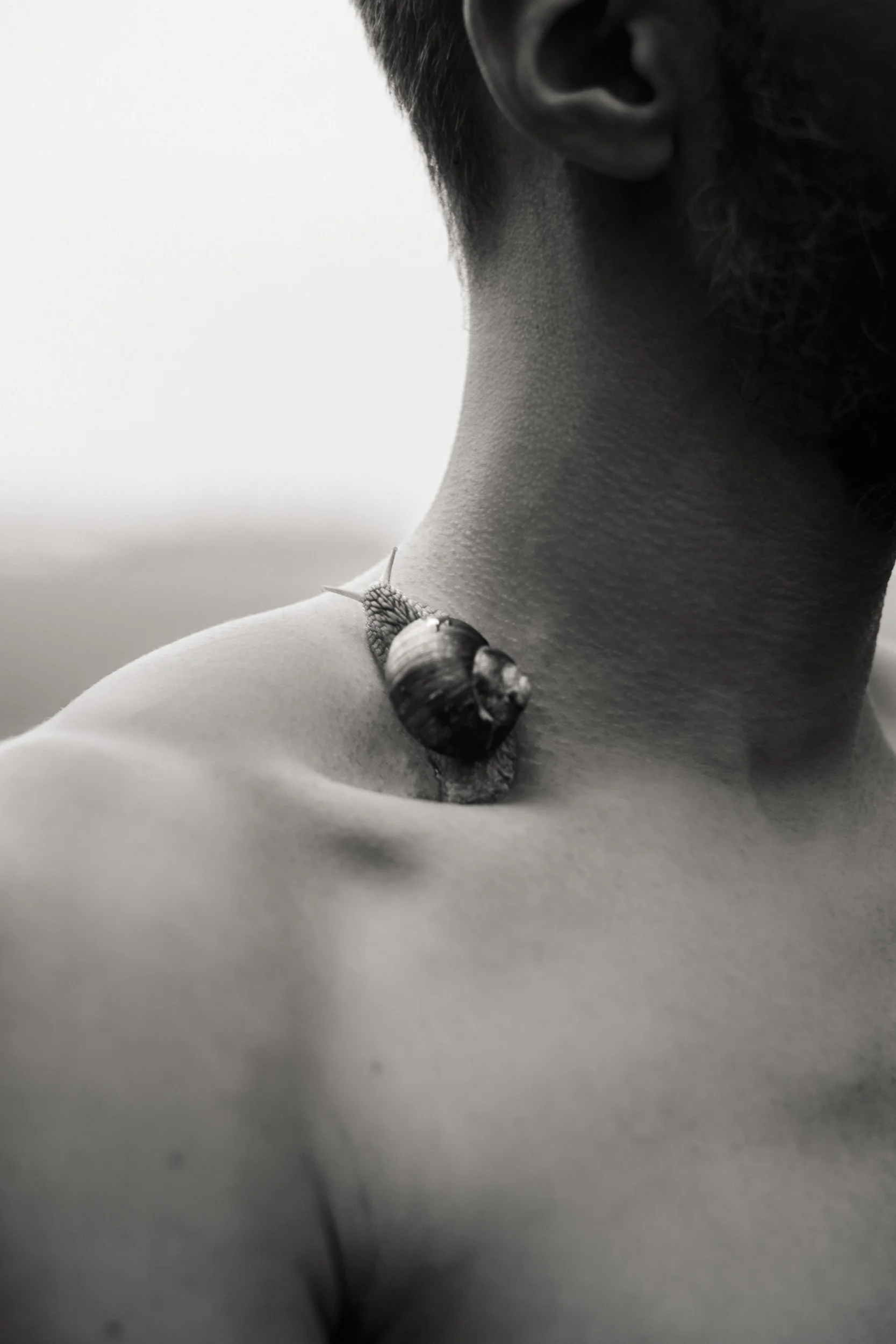 Close-up black and white photograph of a person's neck and shoulder, with a snail on the shoulder.