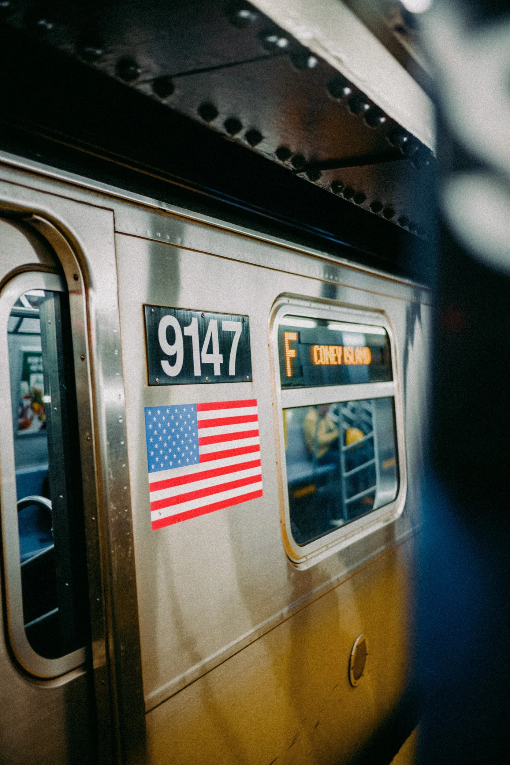 Close-up of the side of a train car with the number 9147, an American flag sticker, and a digital sign showing 'CARRY BAG'.