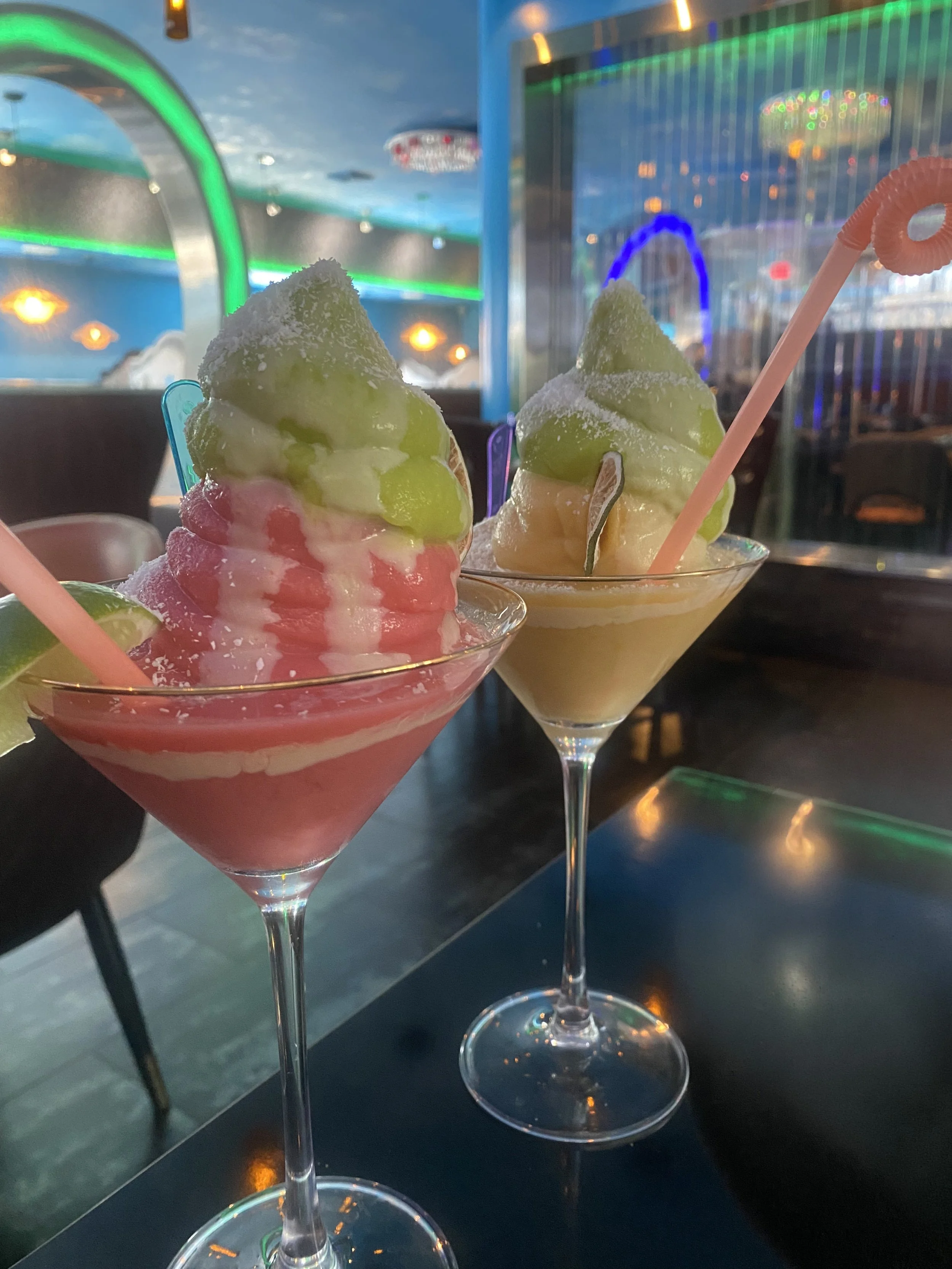 And two multiflavor, soft serve margaritas in glasses with colorful straws, and a lime slice in a very vibrant restaurant.