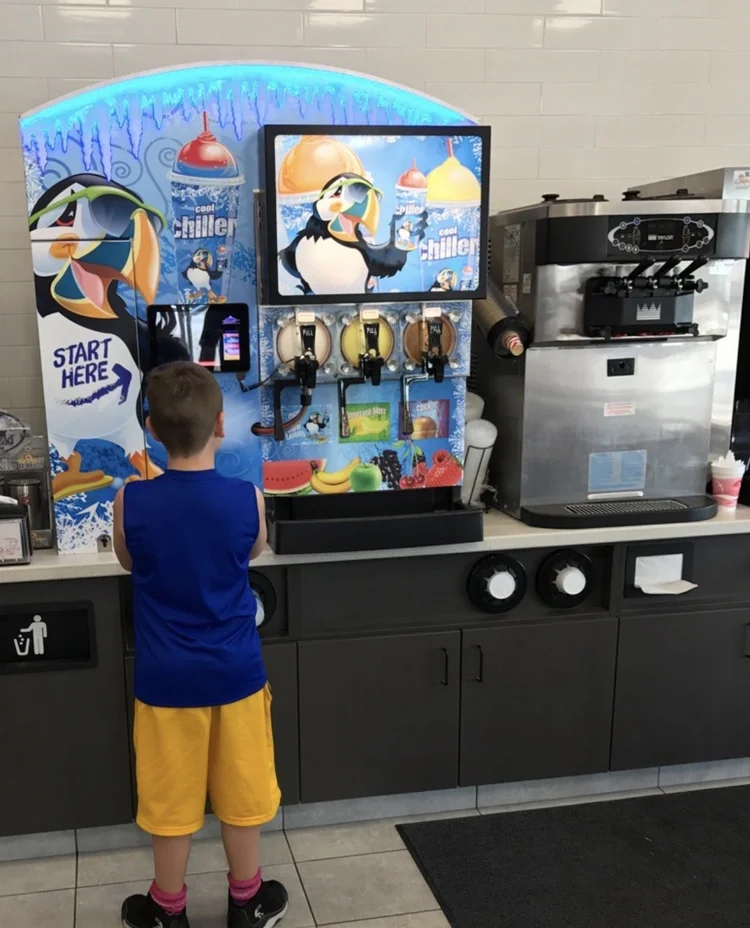 Kid choosing a frozen beverage standing in front of a machine with 3 spouts