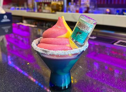 soft serve margarita in a blue salted rim cup with red and yellow maragarita soft serve and a mini bottle of tequilla stuffed into the side of the soft serve.