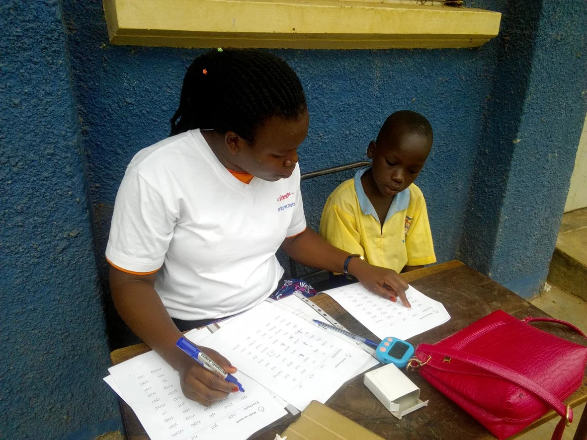 Teacher Diana from St Michael's Kindergarten and Primary assessing the reading of a pupil in Negri Primary School, Gulu. 