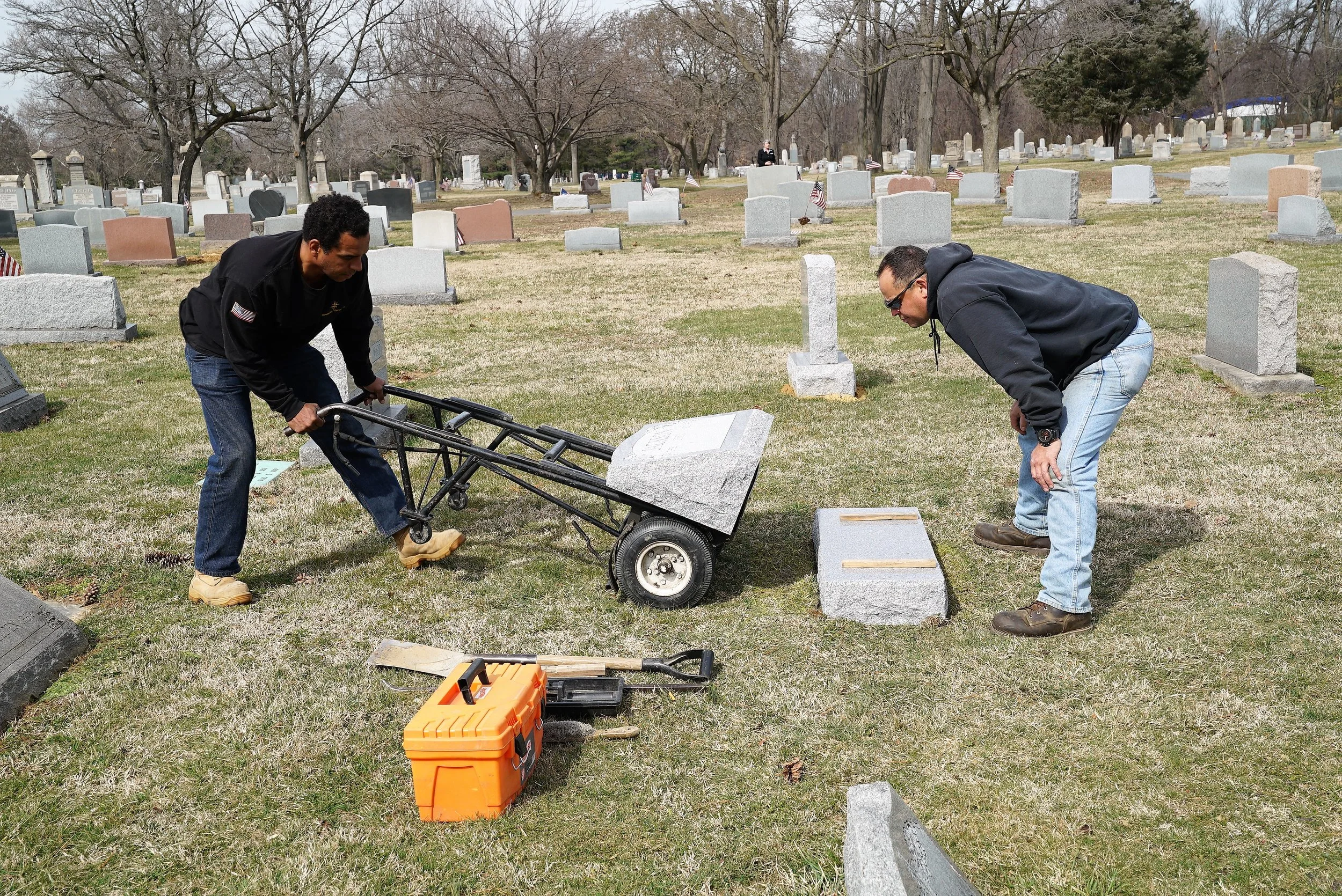 Workers setting a headstone at Lawn Croft Cemetery in Marcus Hook, PA. A cemetery representative exercises attention to detail as she watches from a distance.