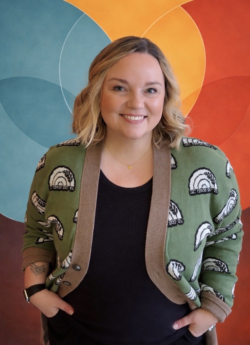 renee sommer facilitator with blonde wavy hair, black shirt and rainbow cardigan against a colorful background