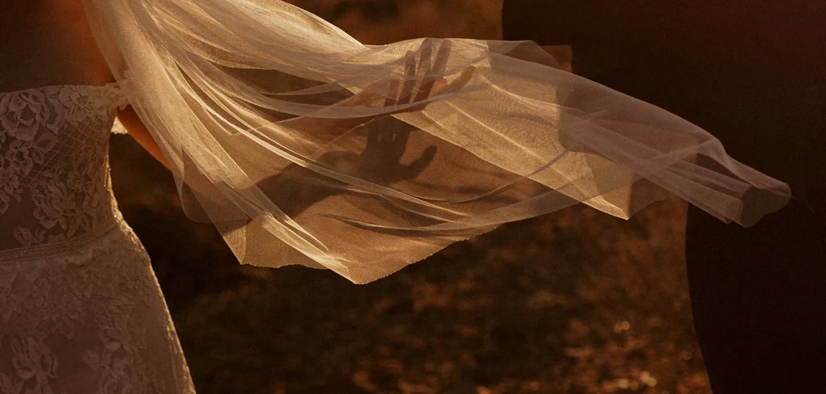 Close-up of a bride's lace wedding dress and veil, with hand shadows at sunset.