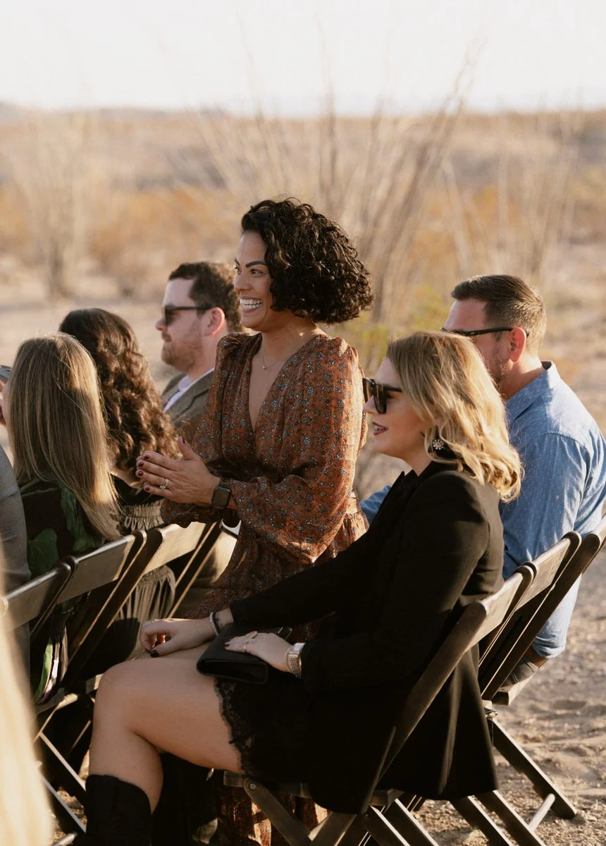 People sitting outdoors on folding chairs, smiling and engaged."}