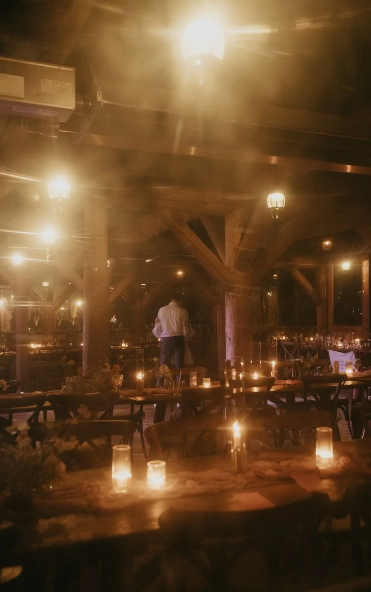 Dimly lit rustic wedding reception with candles on tables and a couple dancing.